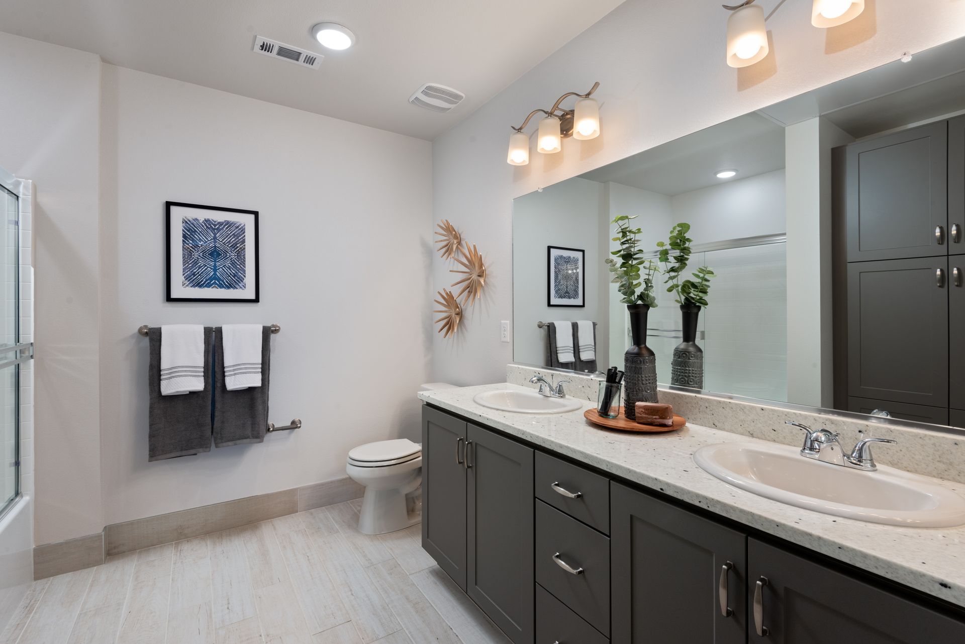 Spacious bathroom with double vanity, grey cabinets, large mirror, and artwork on the wall.