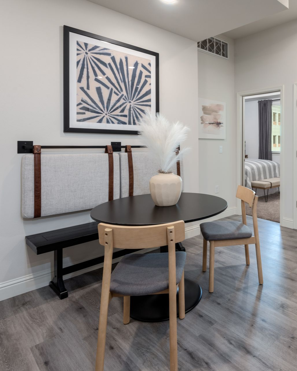 Dining area: Black oval table, bench, two chairs, and art on a gray-floored room.