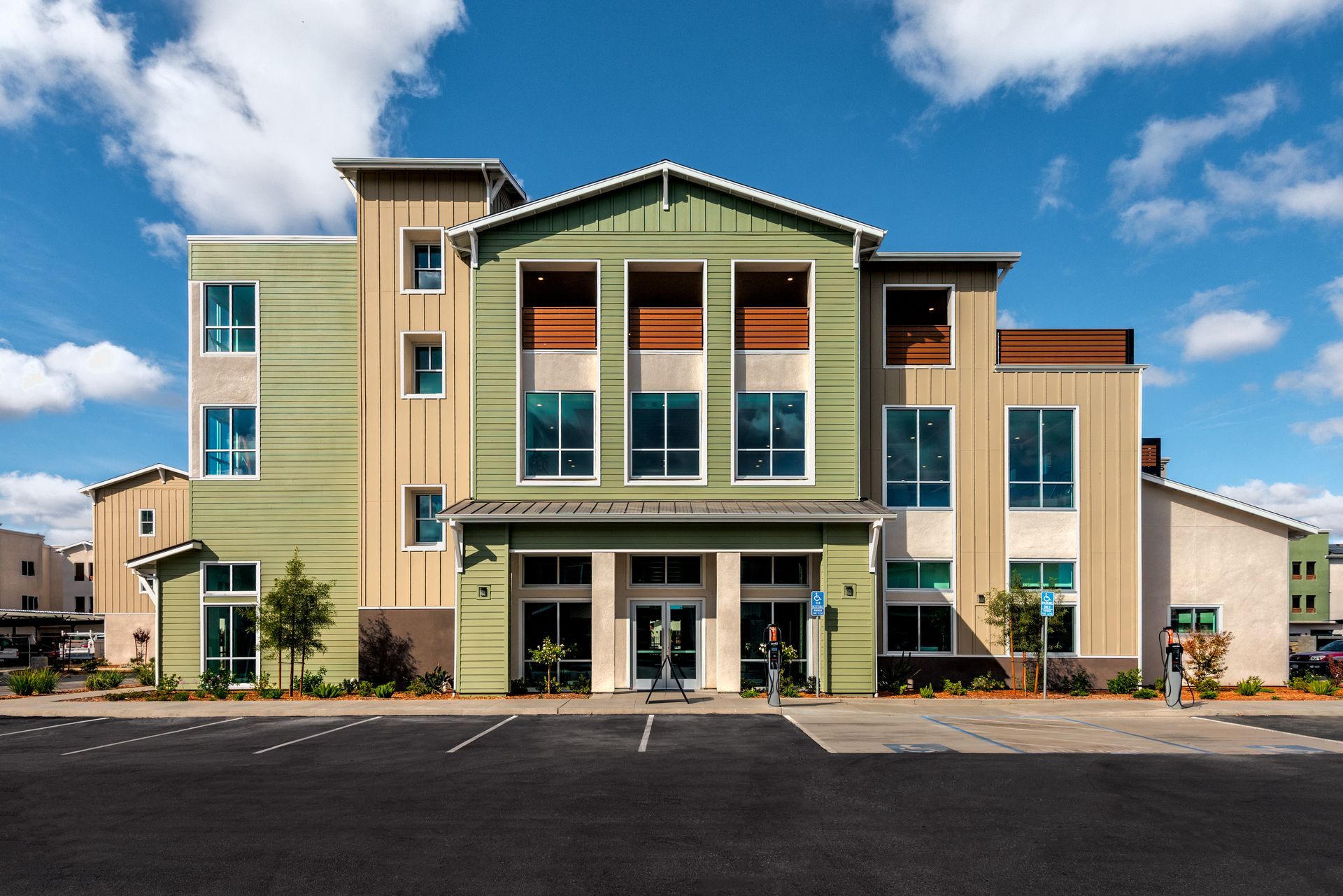 Multi-colored building with blue sky background. Main entrance with glass doors and a parking lot.