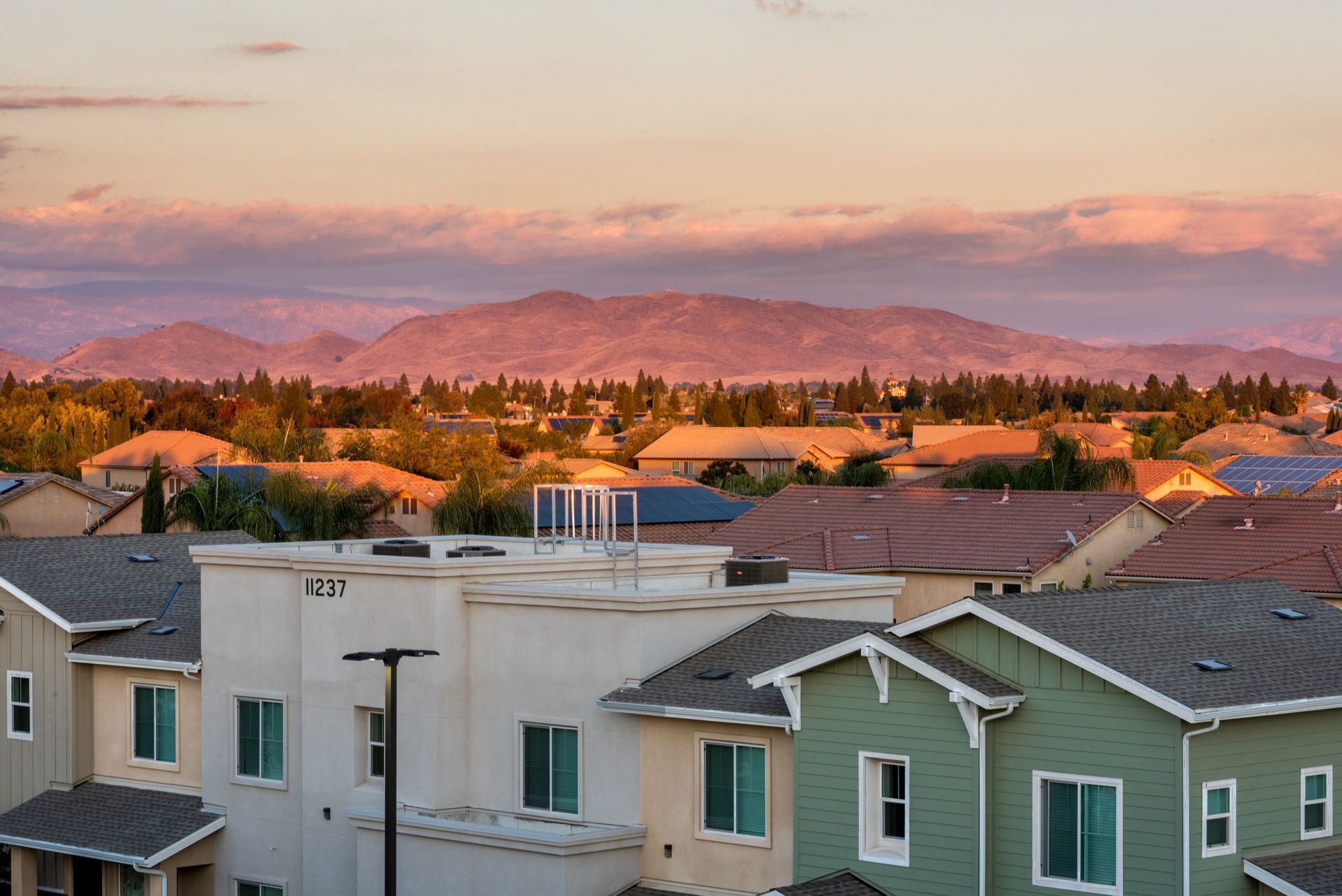 Houses with rooftops against a backdrop of mountains and a colorful sunset.