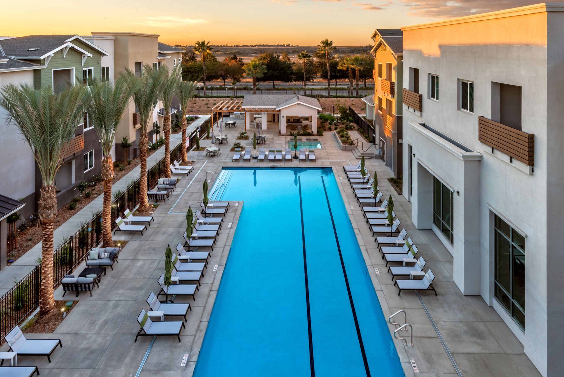 Pool and lounge chairs between two buildings with a sunset in the background.