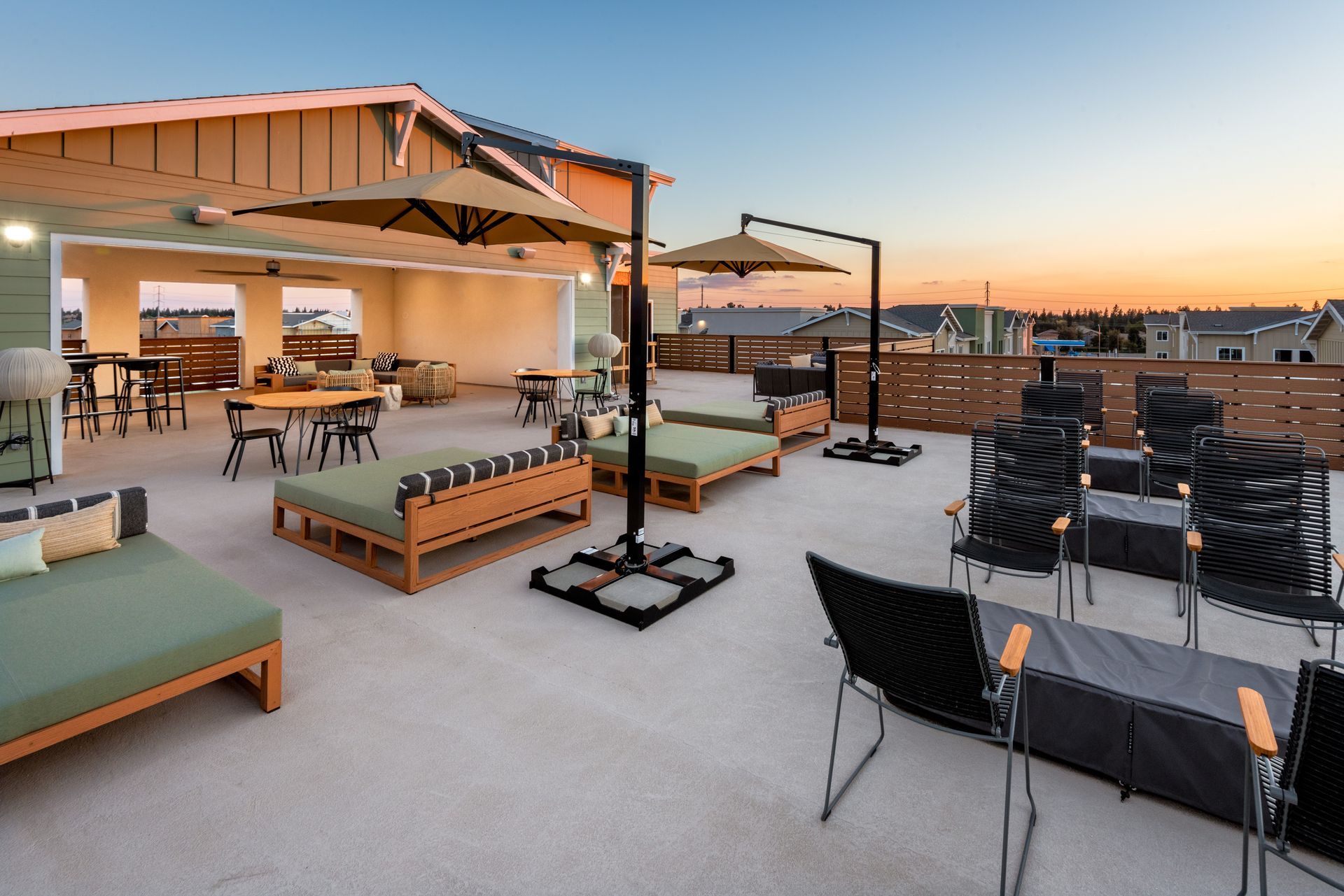 Rooftop lounge with shaded seating, including couches and chairs, overlooking a cityscape at sunset.