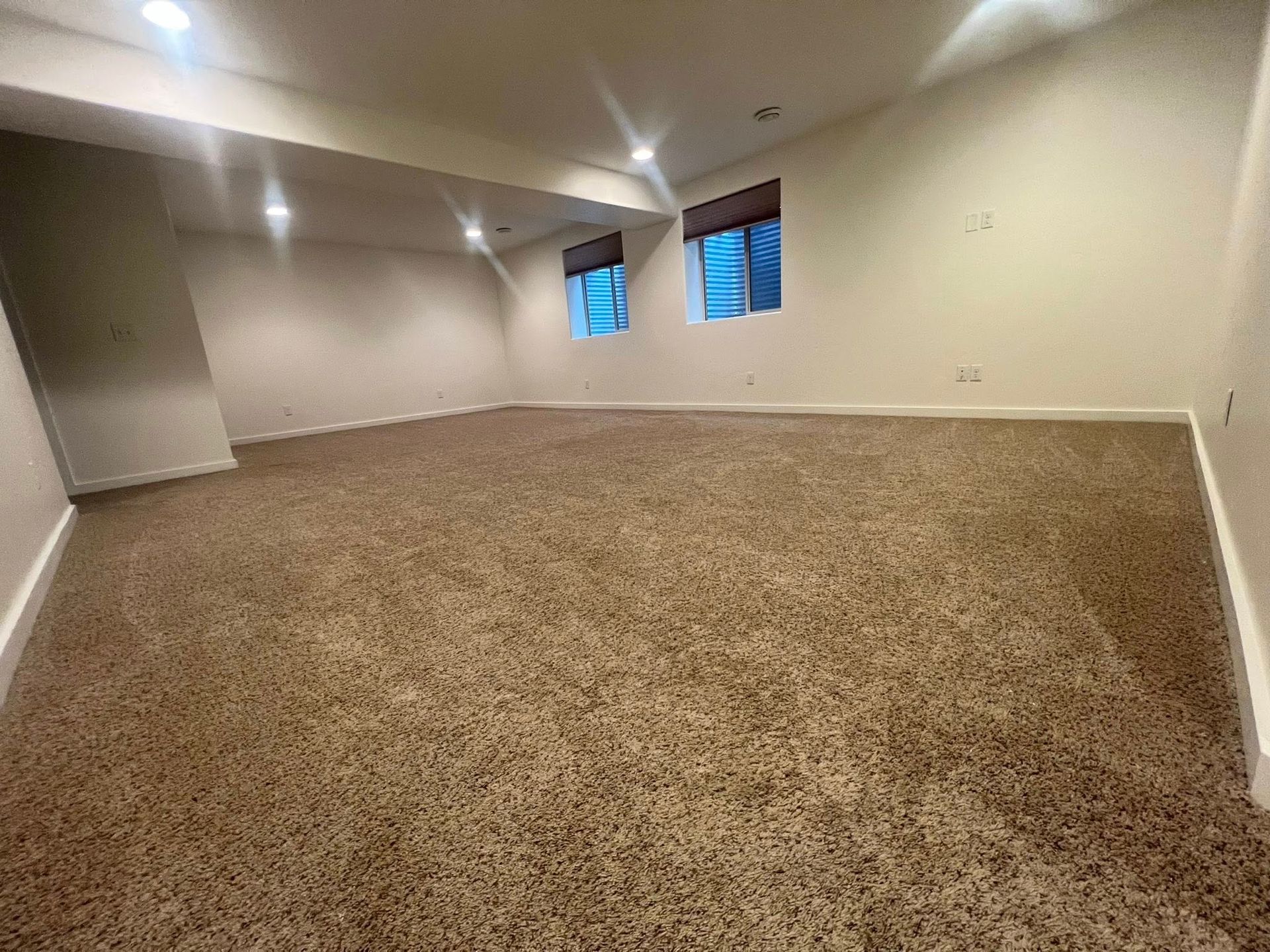 An empty basement with a carpeted floor and two windows.