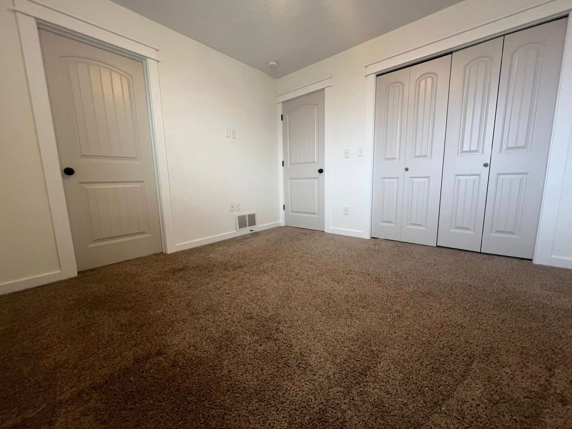 An empty bedroom with a brown carpet and white doors.