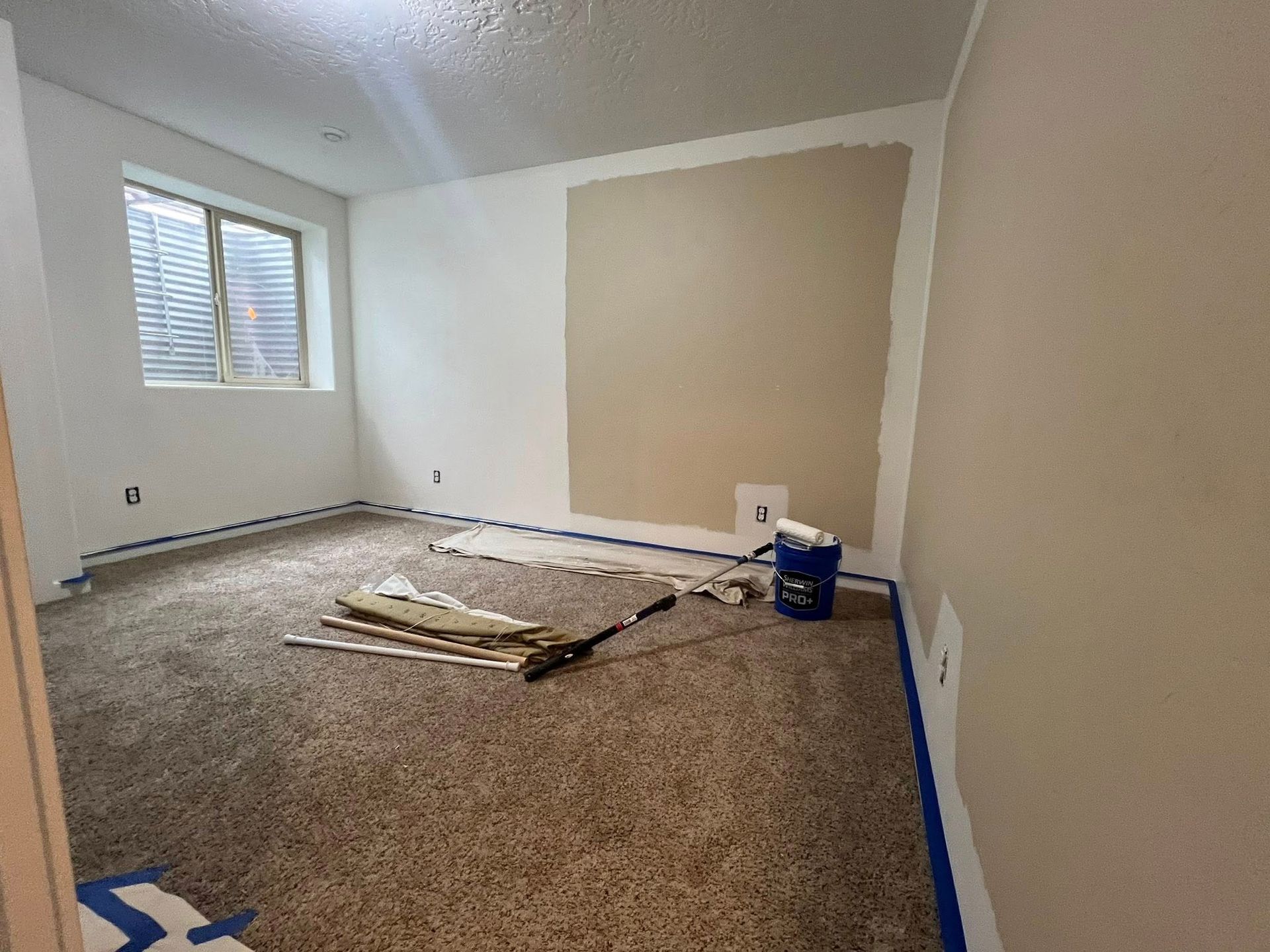 A room with a carpeted floor and white walls is being painted.