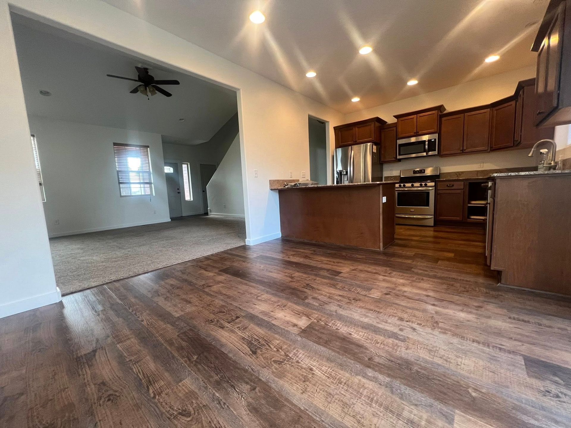 A kitchen with wooden floors , stainless steel appliances , and a ceiling fan.