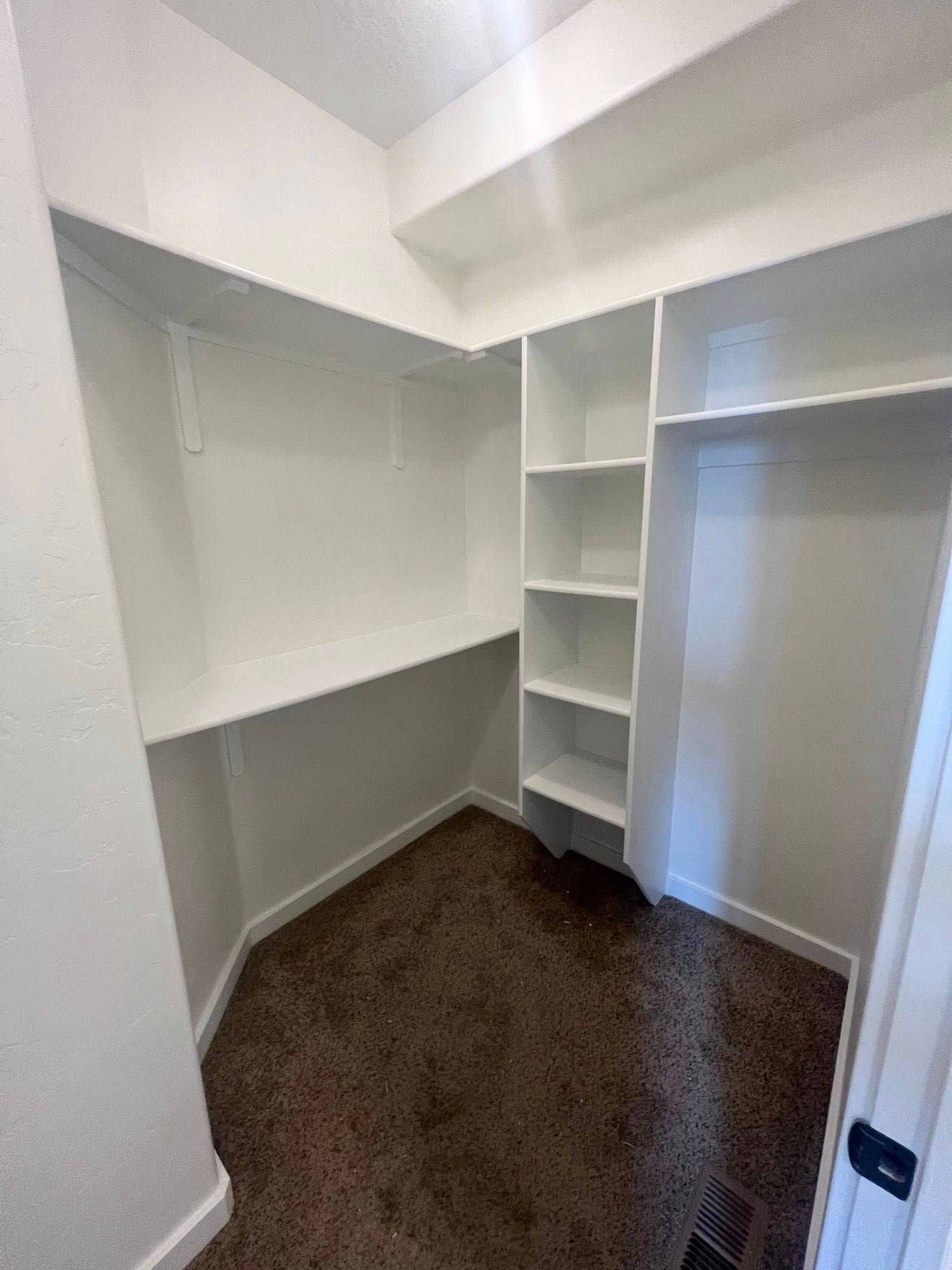 A walk in closet with lots of shelves and a brown carpet.