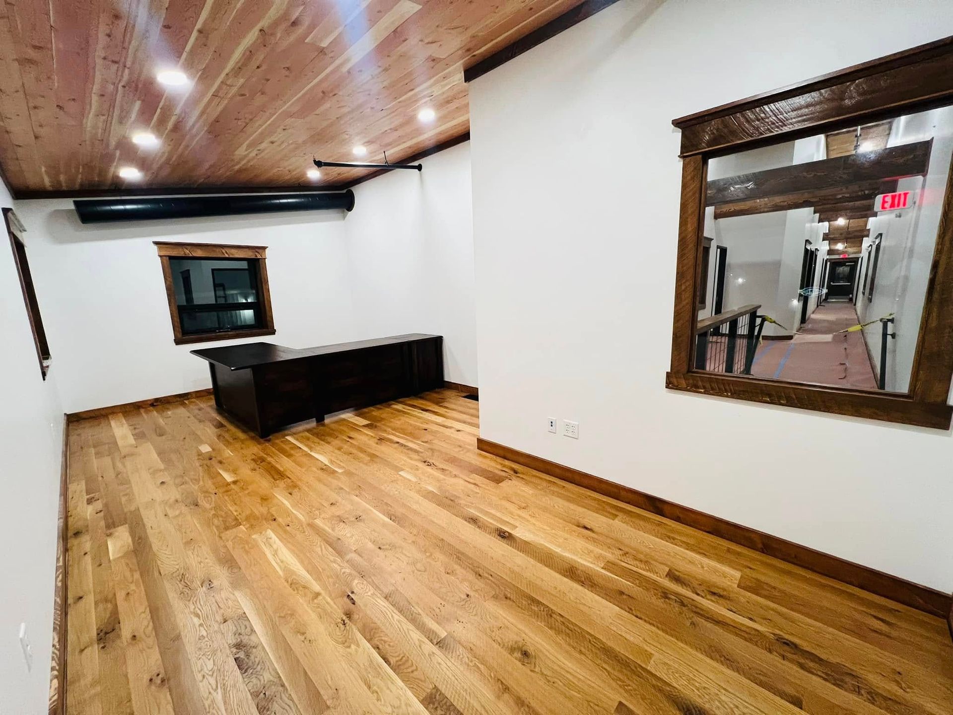 A room with hardwood floors , a desk , and two windows.