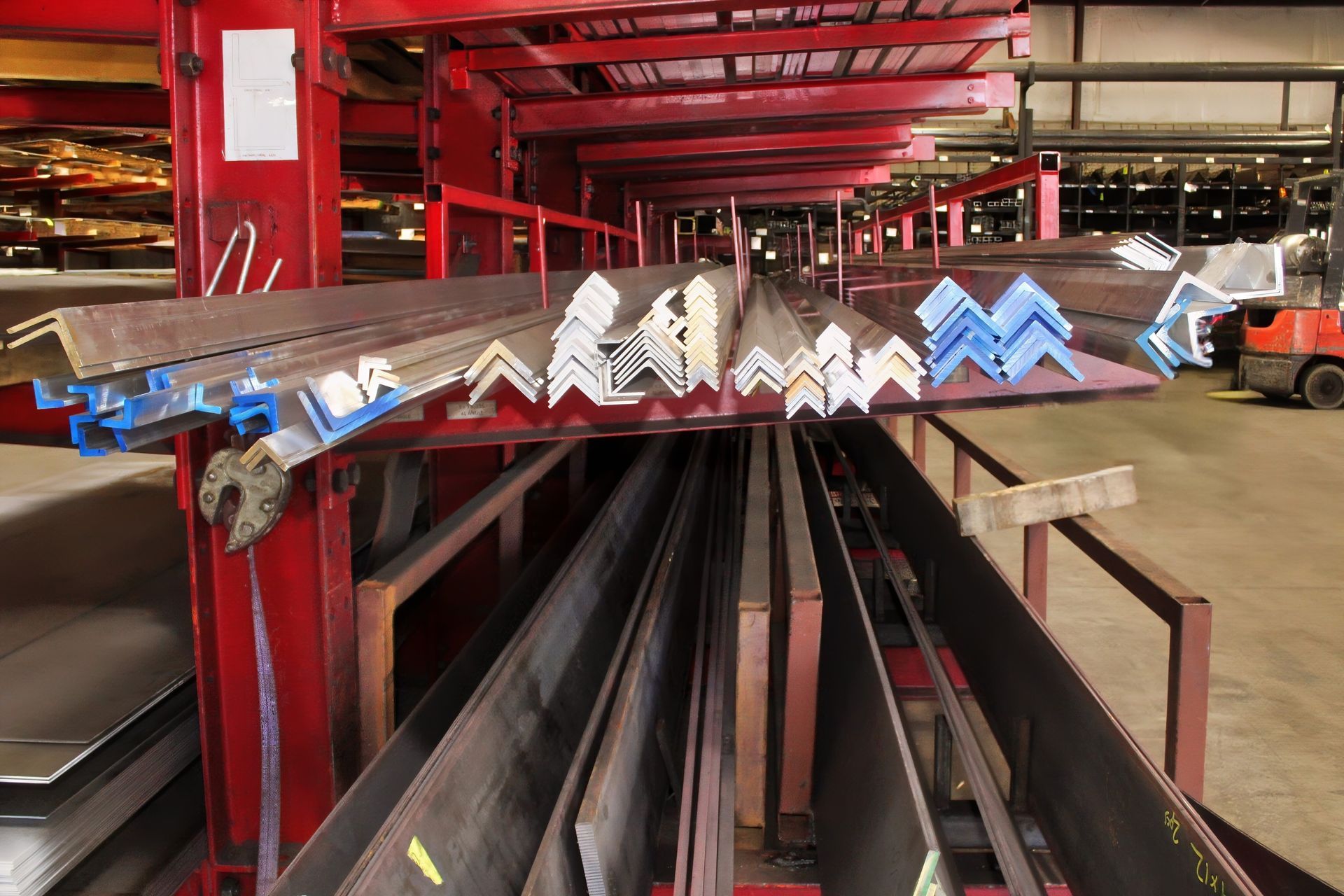 Metal angles and flat sheets stored on red industrial shelving.