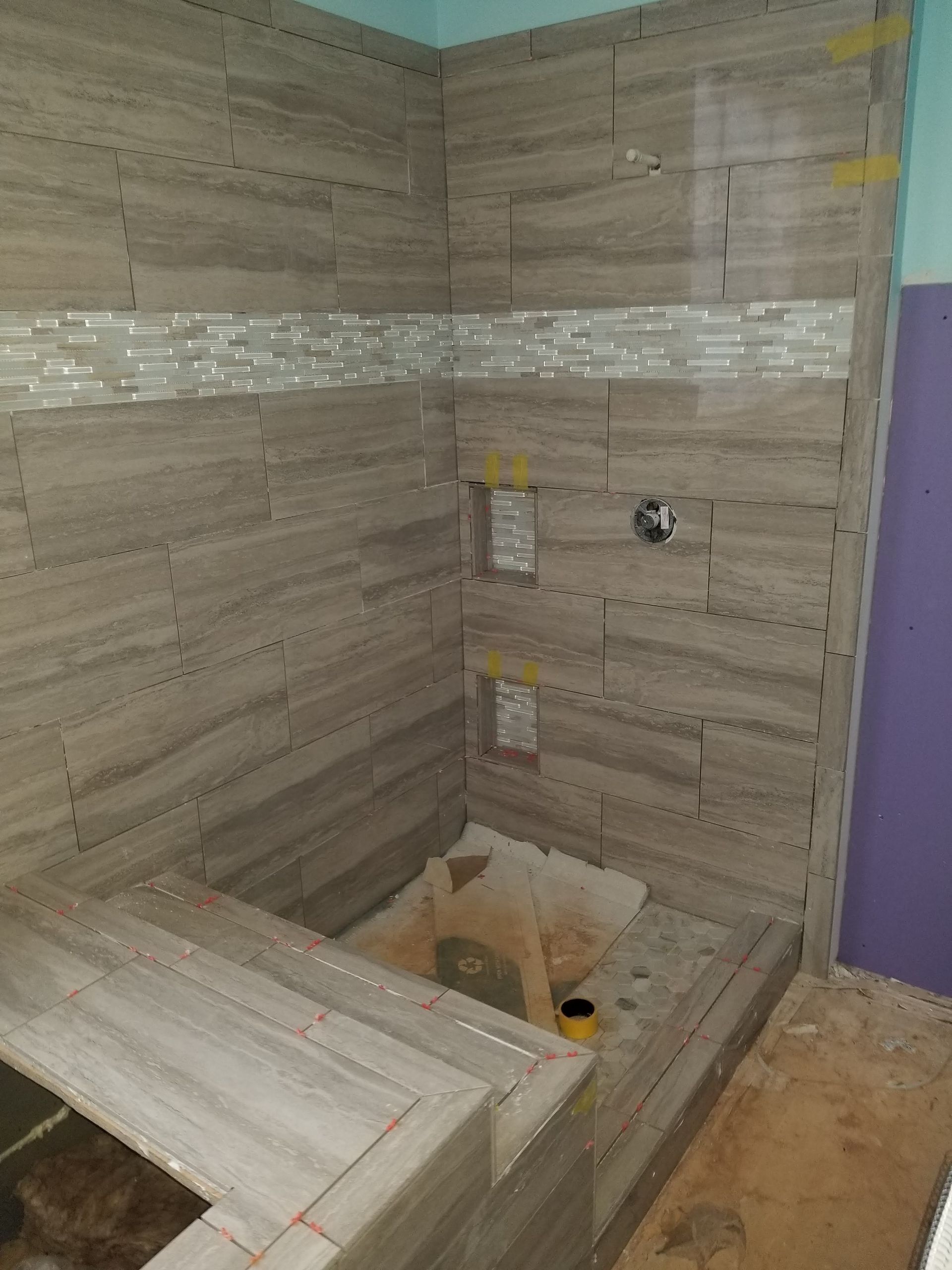 A bathroom with tiled walls and a shower stall under construction.