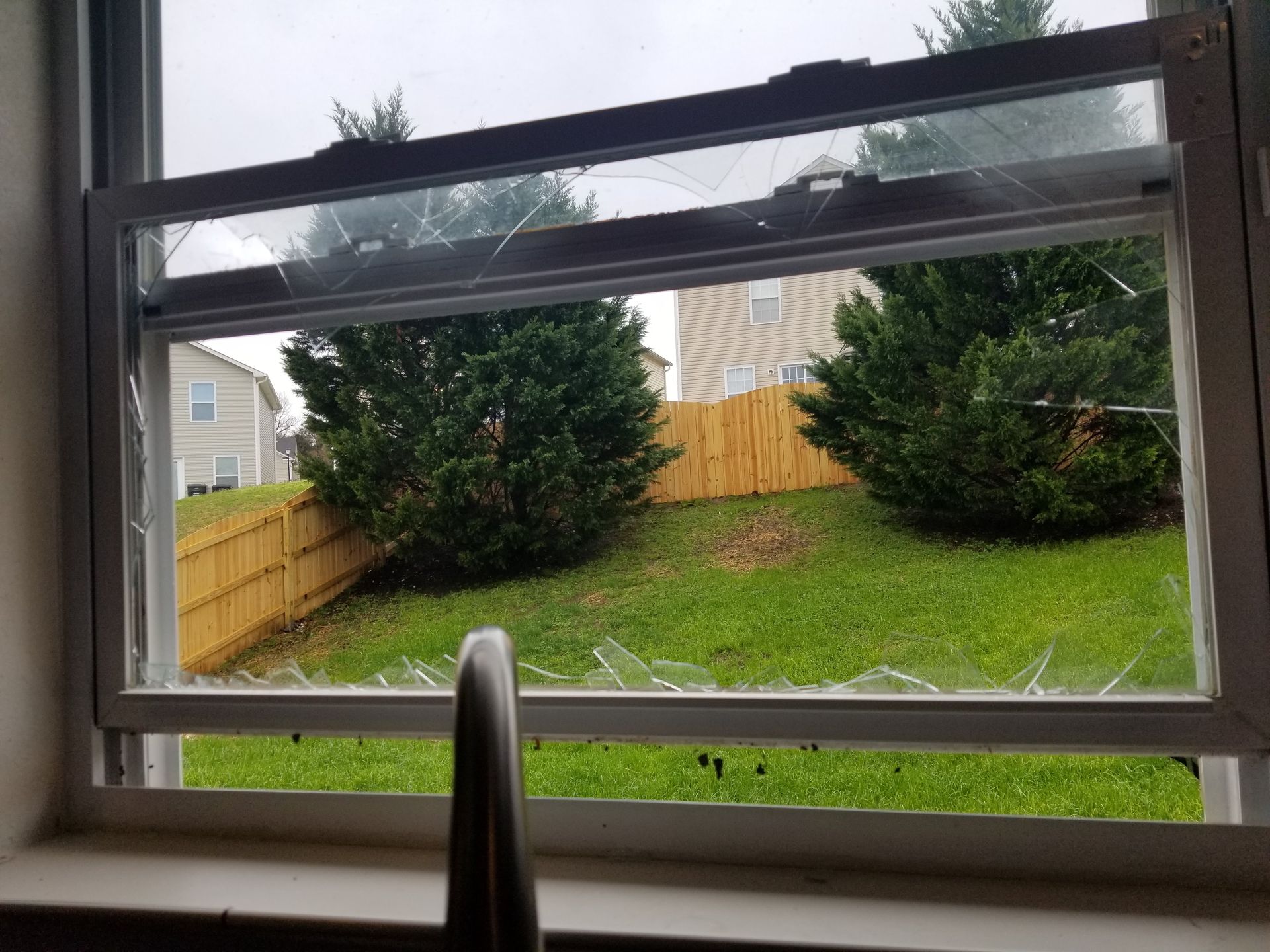 A broken window with a view of a backyard and a fence.