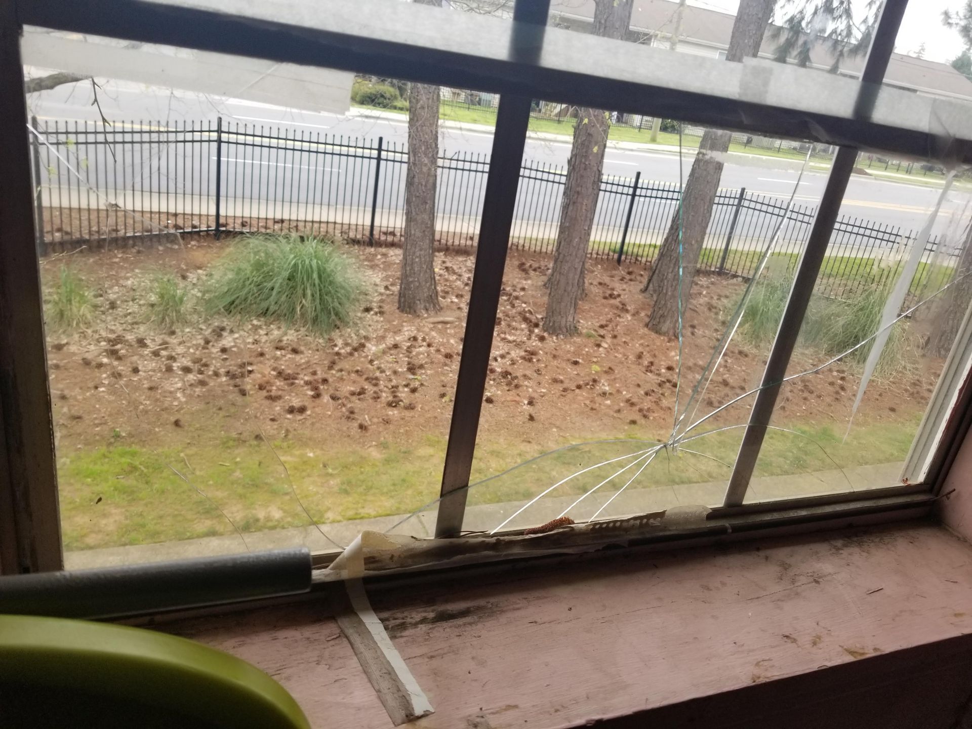 A broken window with a view of a fence and trees