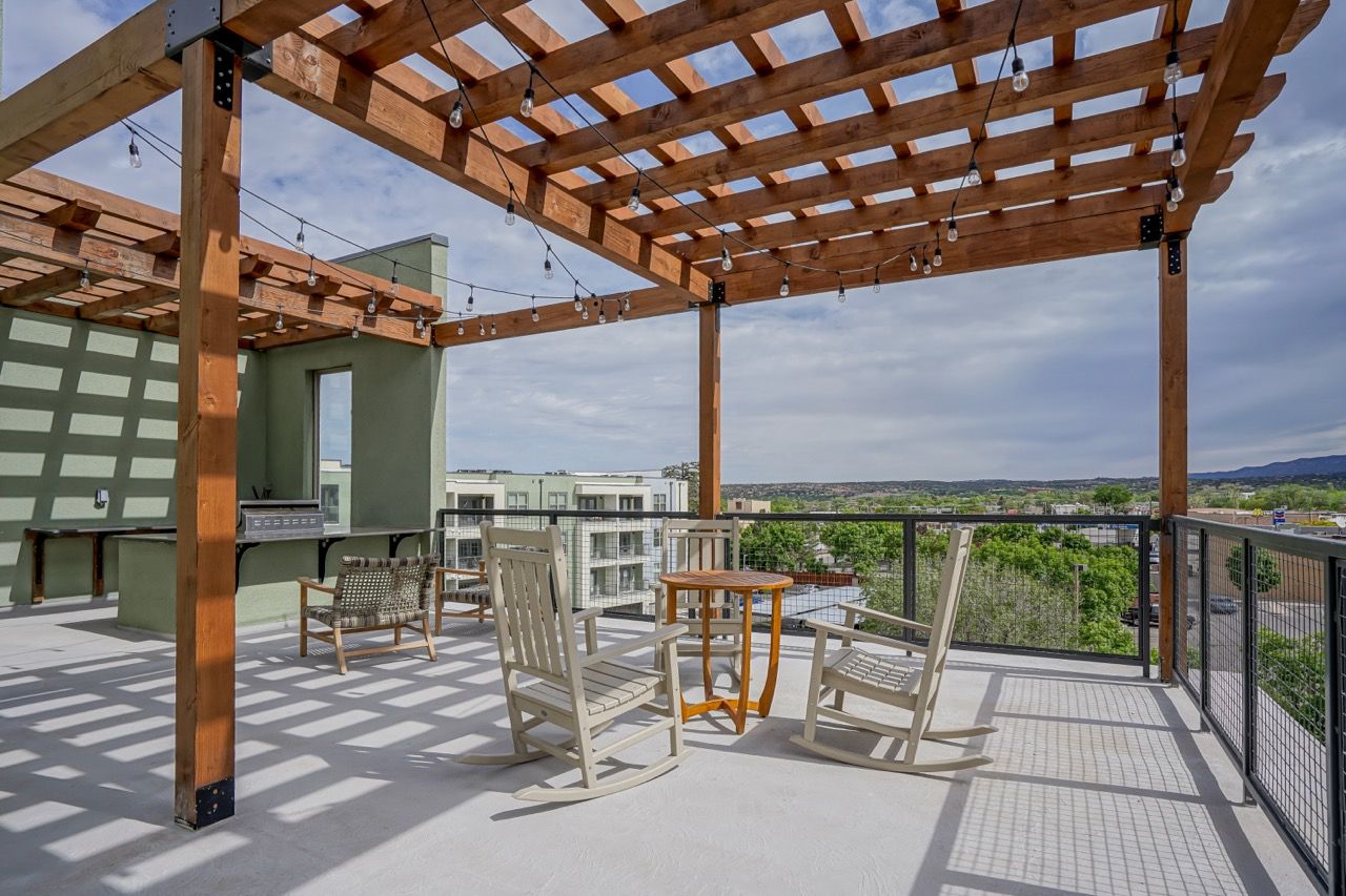 Rooftop terrace with a wooden pergola, string lights, grill, and outdoor seating.