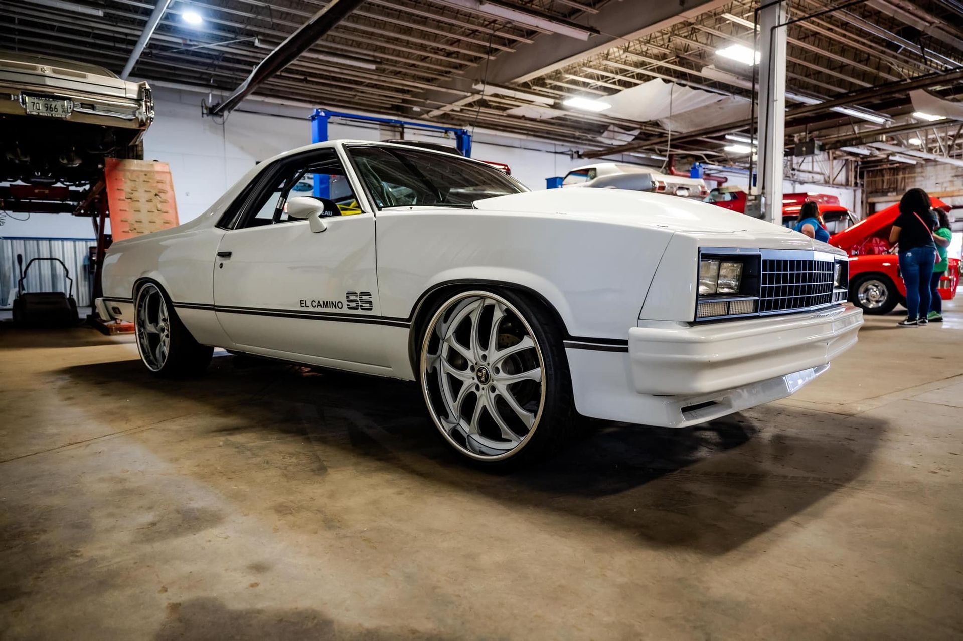 White classic El Camino pickup truck with custom chrome wheels in a garage setting.