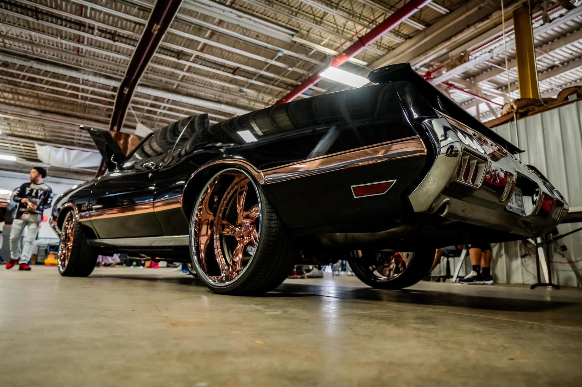 Black classic car with copper wheels on display in a large indoor space.
