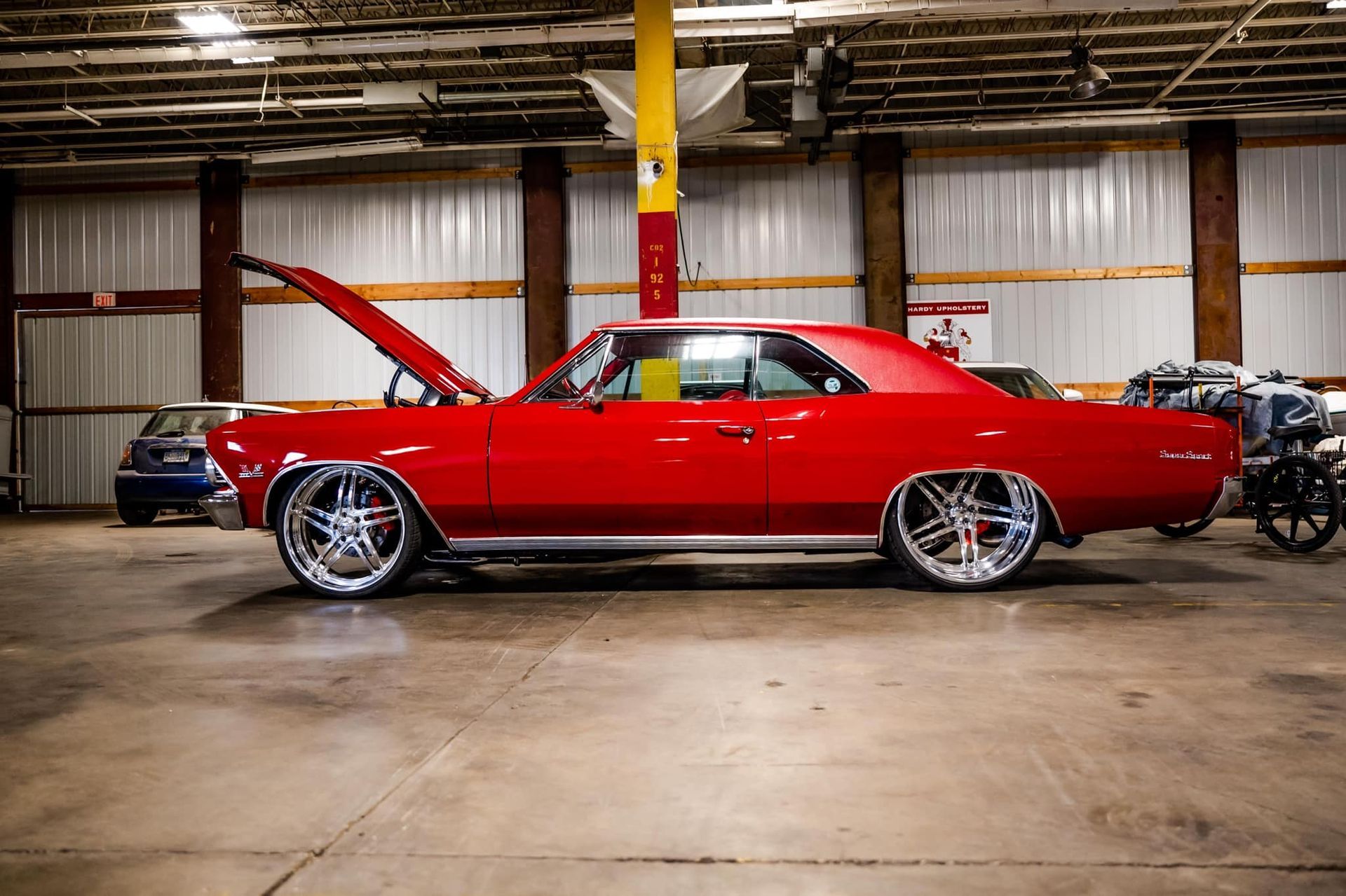 Red classic car with open hood, shiny wheels, inside a large building.