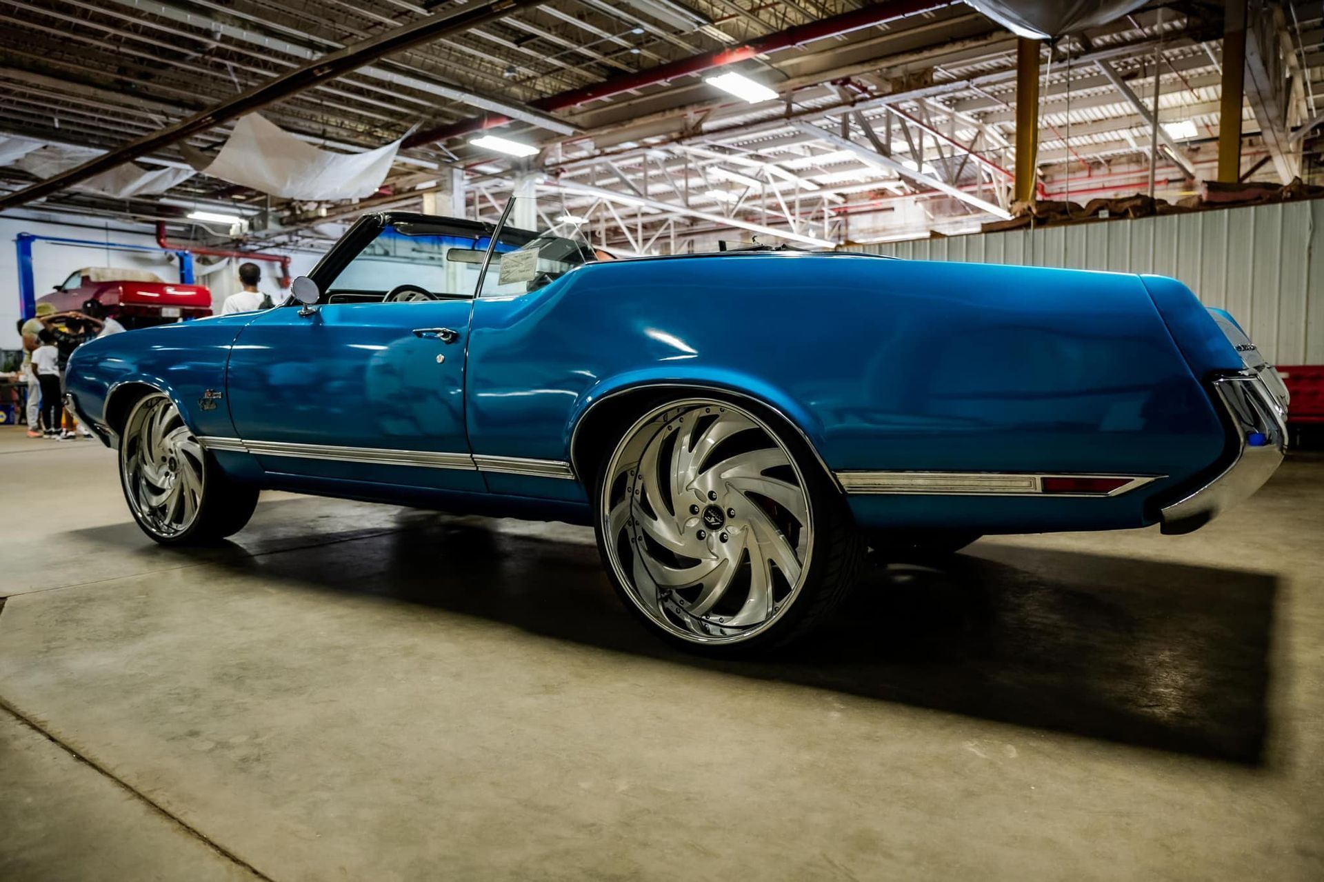 Blue custom convertible car with large chrome wheels in a garage.
