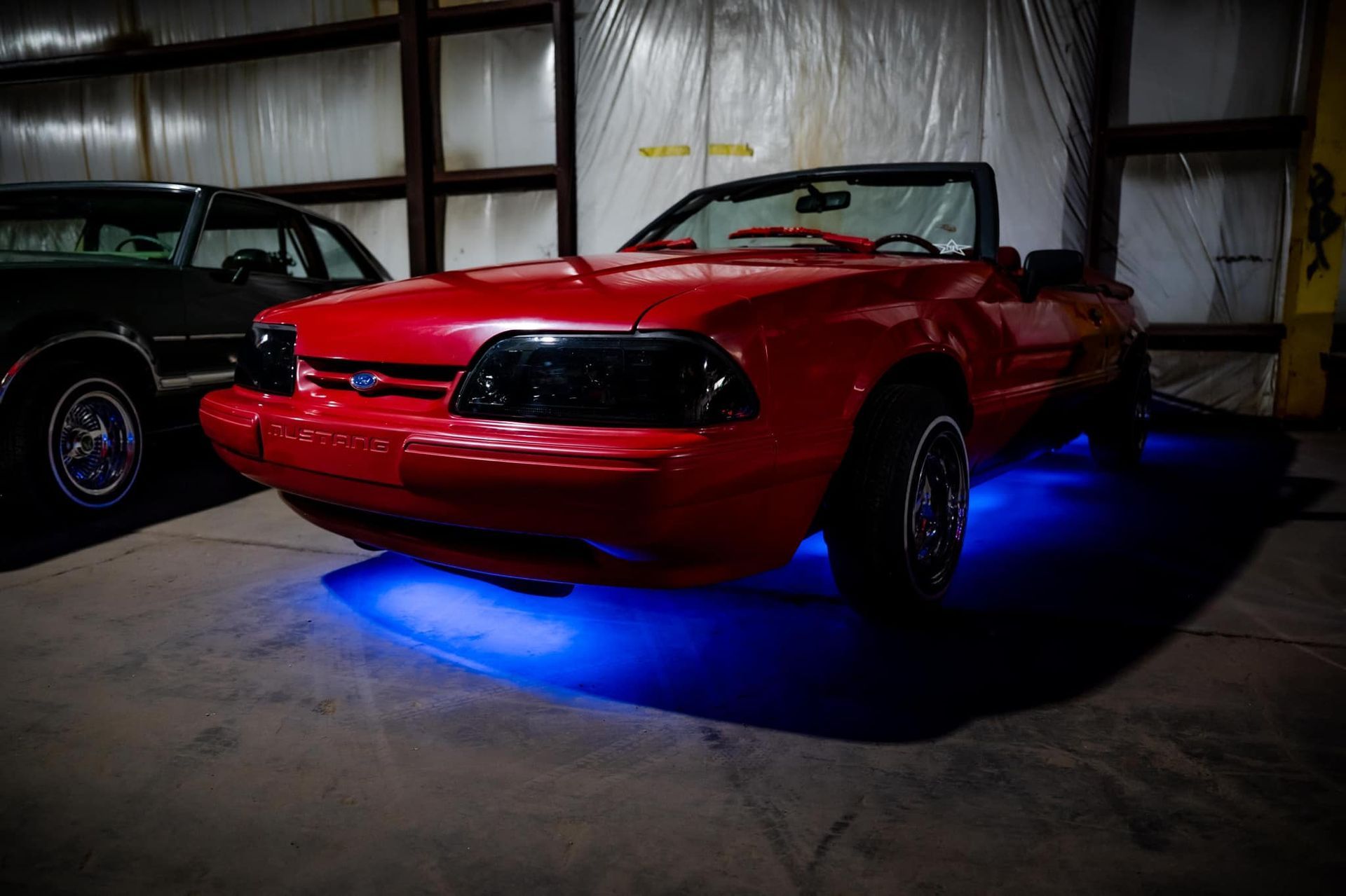 Red Ford Mustang convertible with blue underglow in a garage.