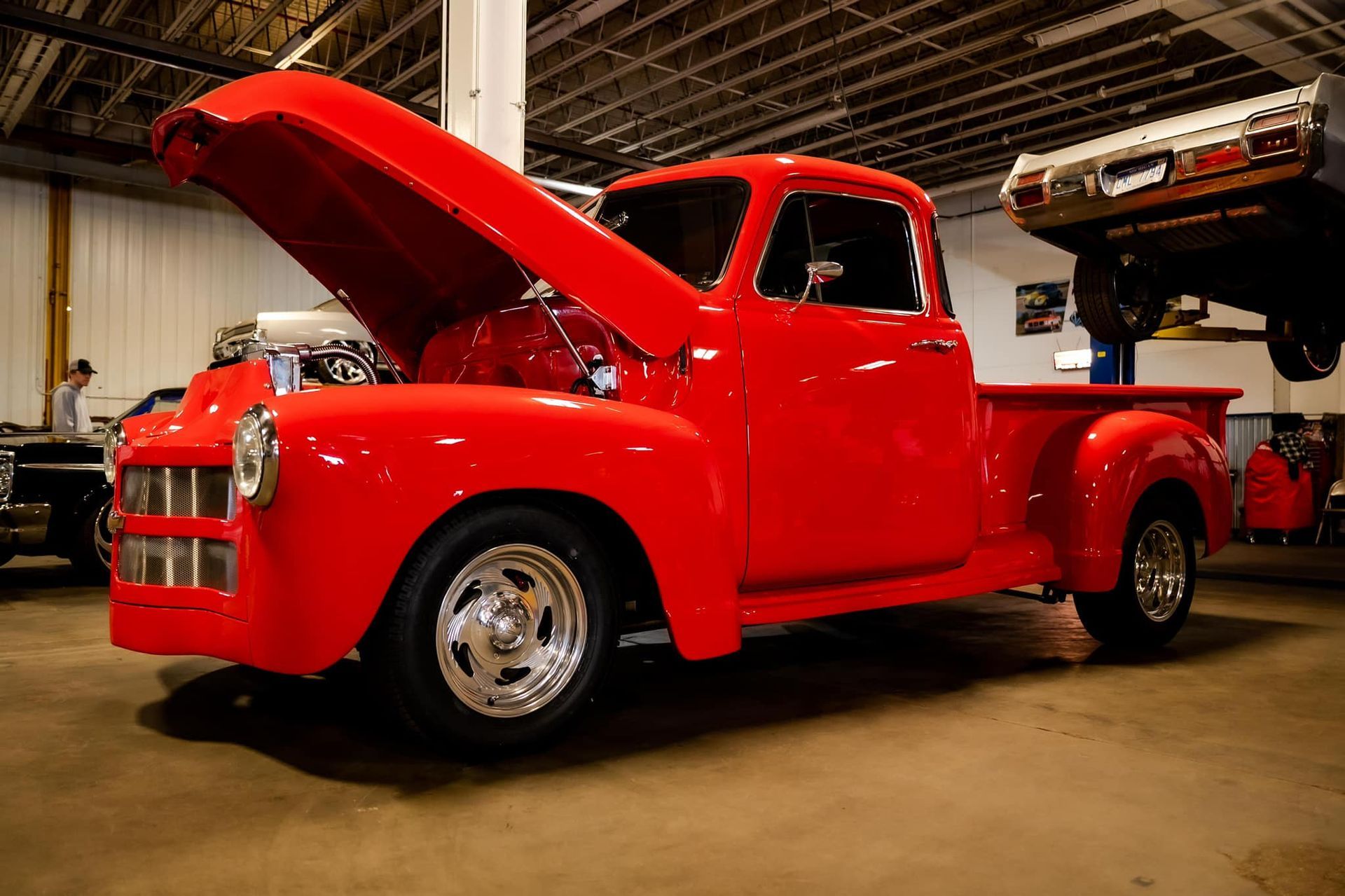 Red vintage pickup truck with the hood open in a garage.