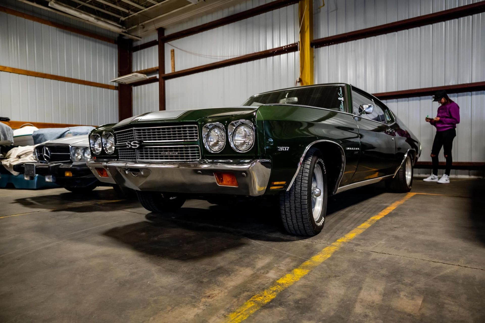 Dark green classic car in a garage with a person looking at their phone.