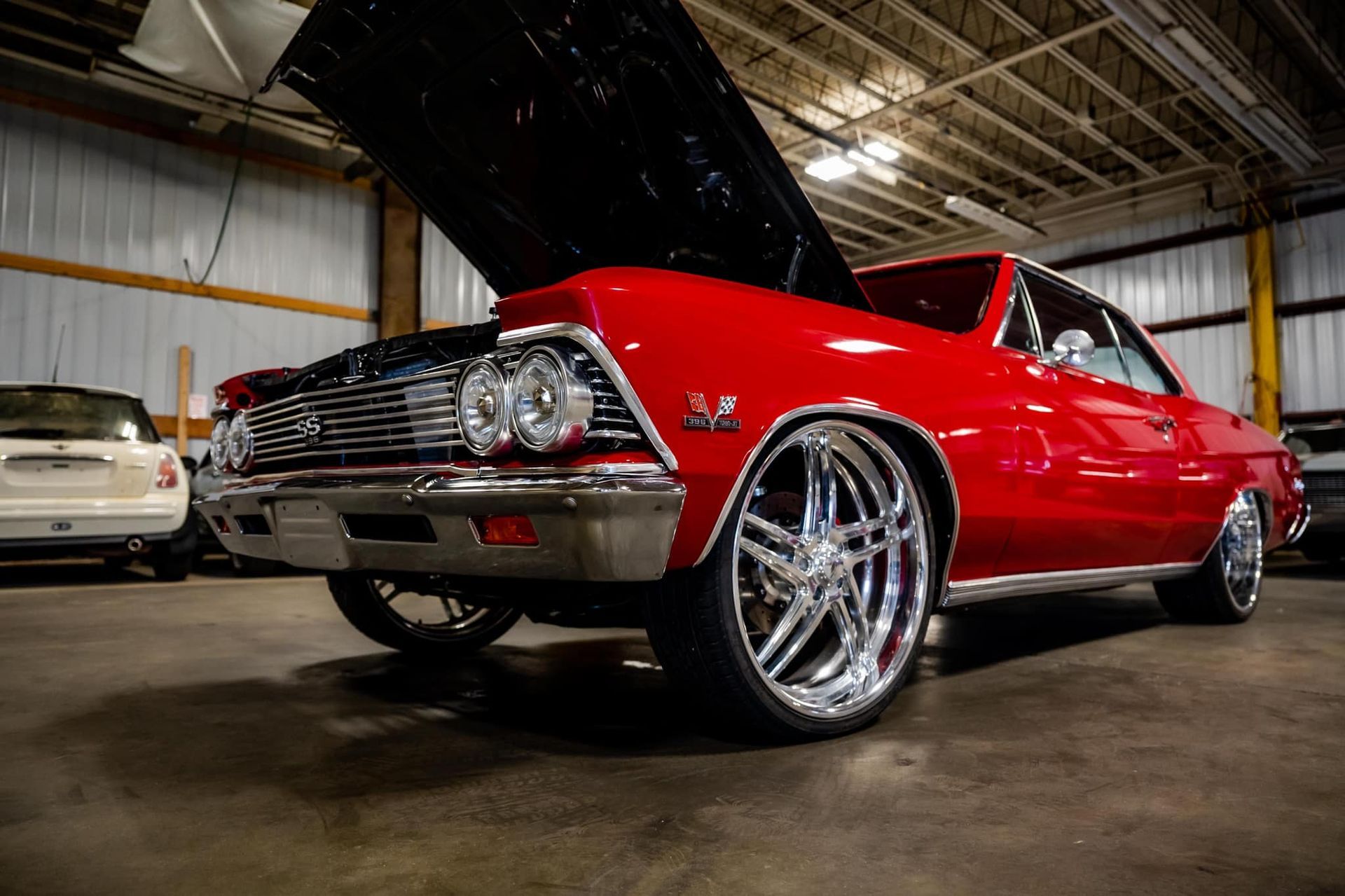 Red classic car with chrome wheels, hood open, inside a garage.