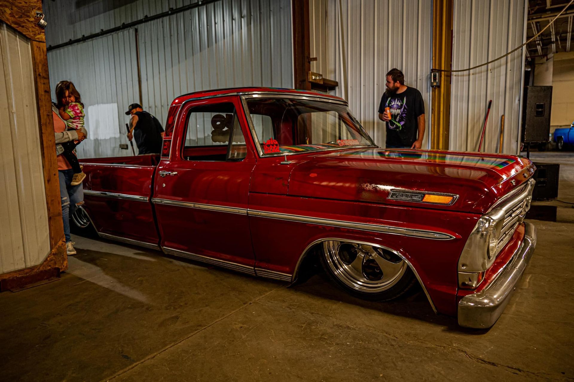 Red classic pickup truck, lowered, indoors; people looking.