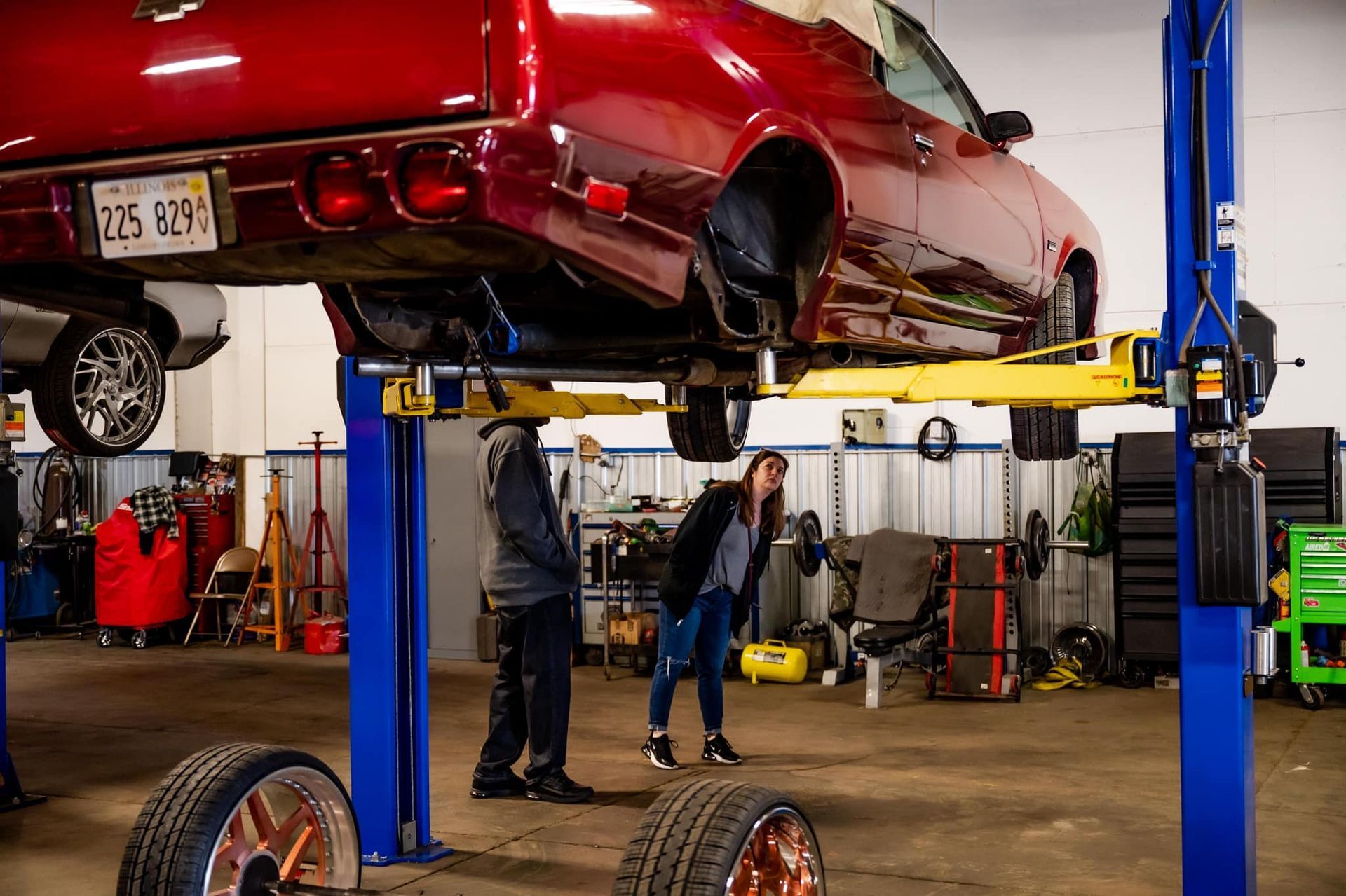 A red convertible on a lift with two people inspecting it in a garage.