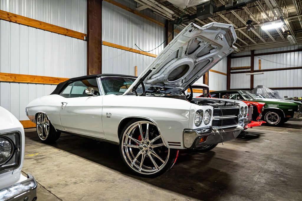 White classic car with hood up, chrome wheels, inside a garage.