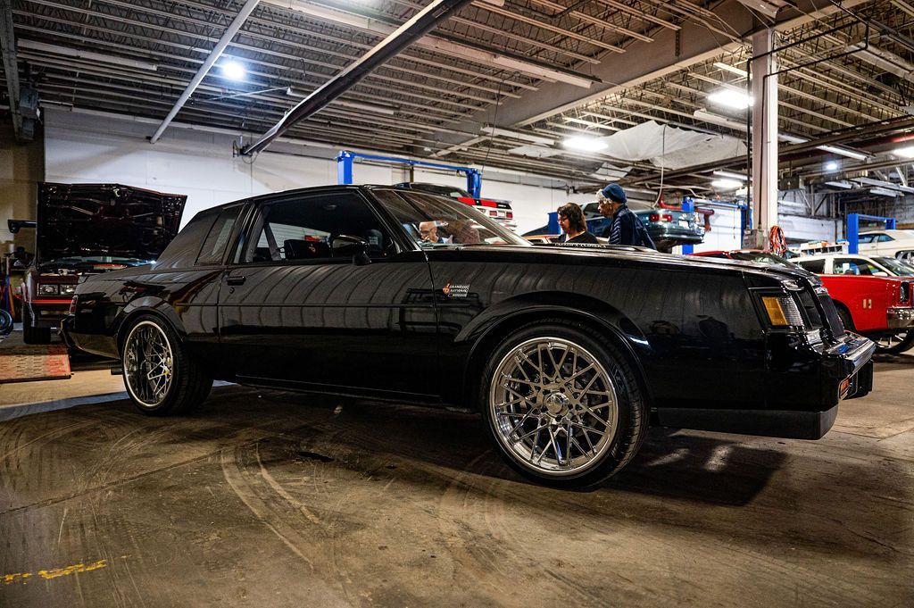 Black Buick Grand National in a garage, chrome wheels, under lights.