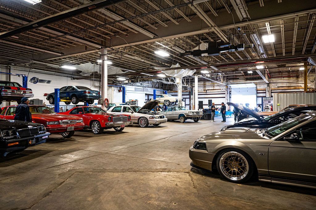 Large garage filled with classic cars, some on lifts. Open bay doors, overhead lights.