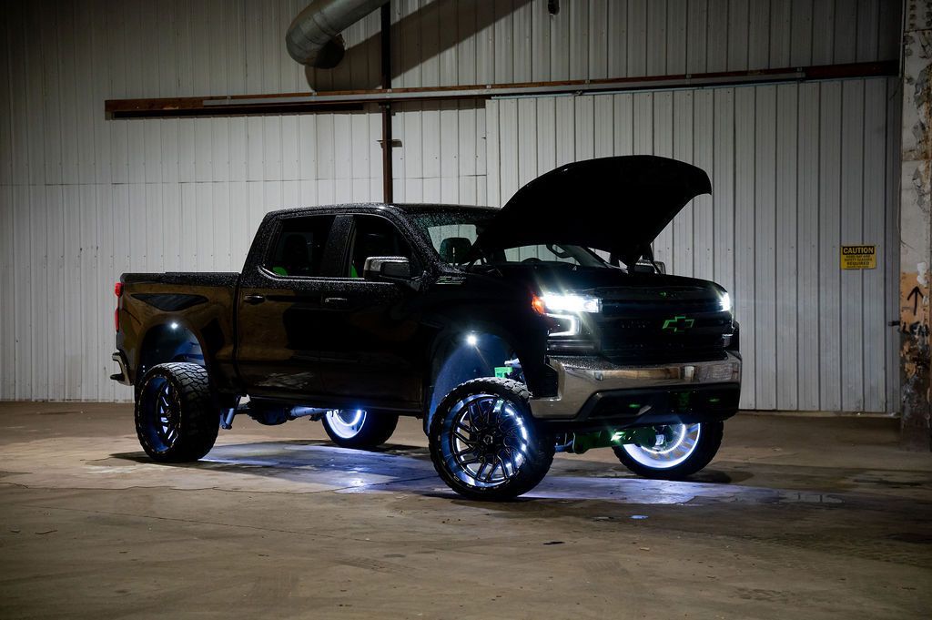 Black lifted truck with LED lights, hood open, in an industrial setting.