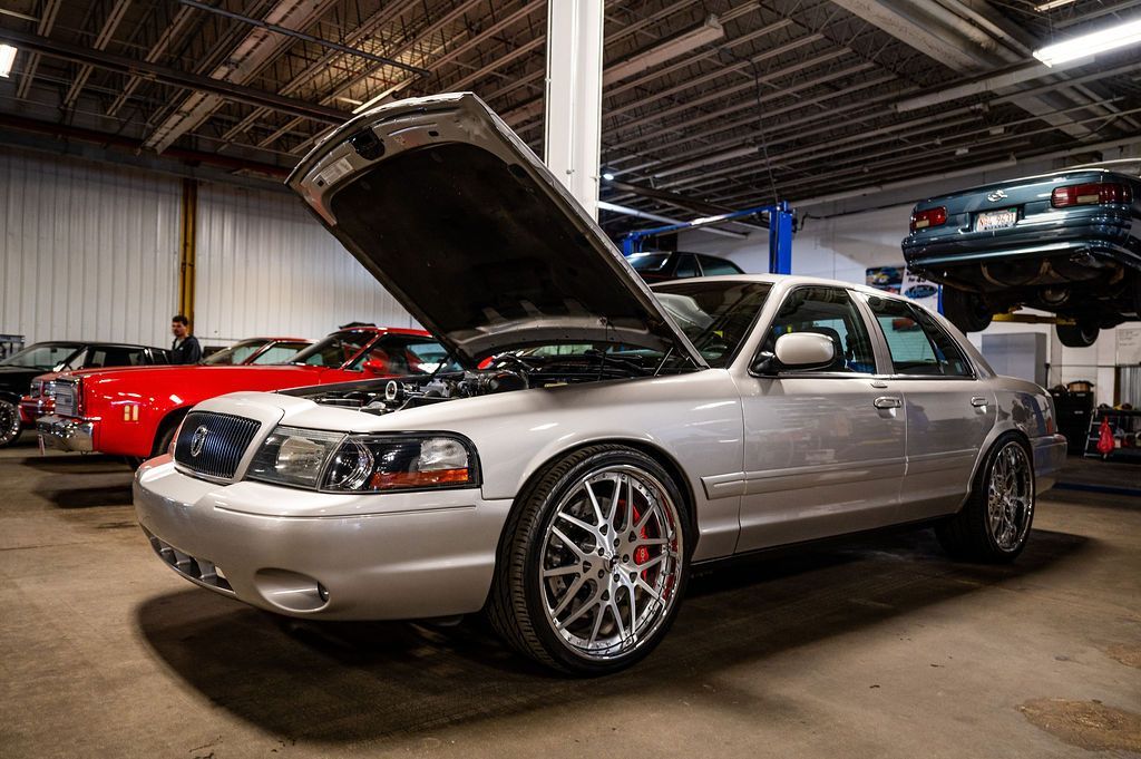 Silver car with hood open in a garage, other vehicles in the background.