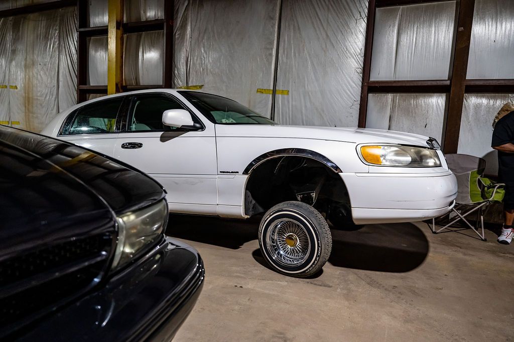 White Lincoln Town Car raised up, parked indoors with other cars; dark car in foreground.