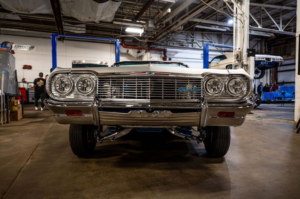 Chrome-detailed lowrider car in a garage, facing the viewer. The car has large headlights.
