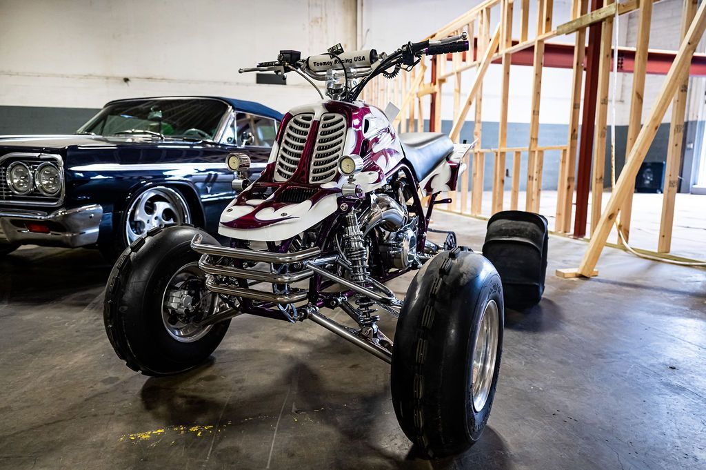 ATV with white and maroon body, parked inside; classic car visible in background.