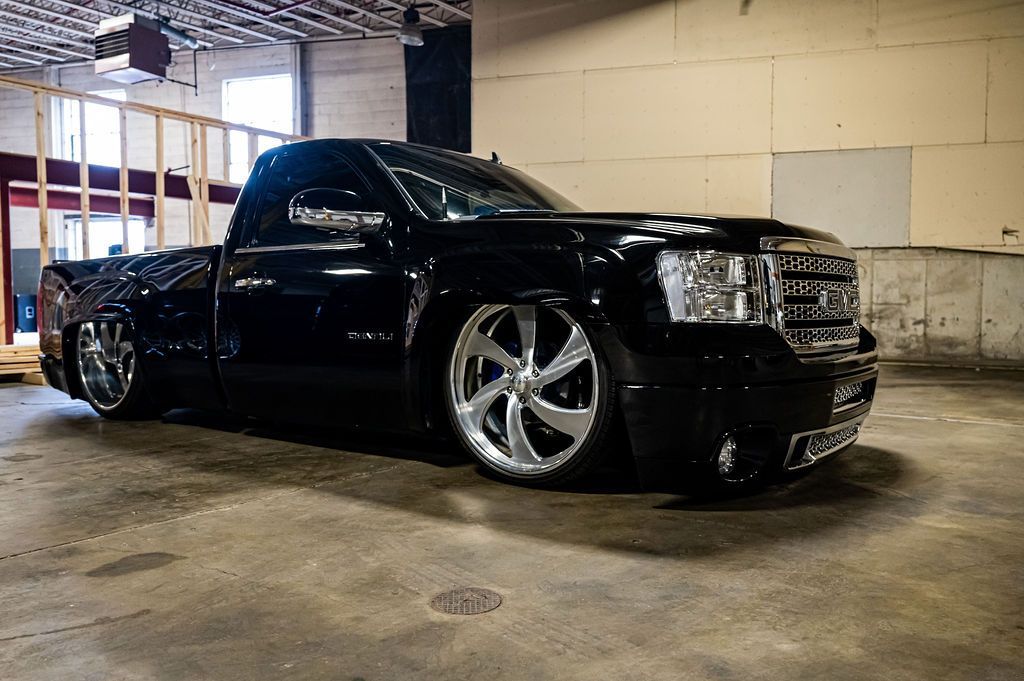 Black lowered pickup truck with chrome rims in a garage setting.
