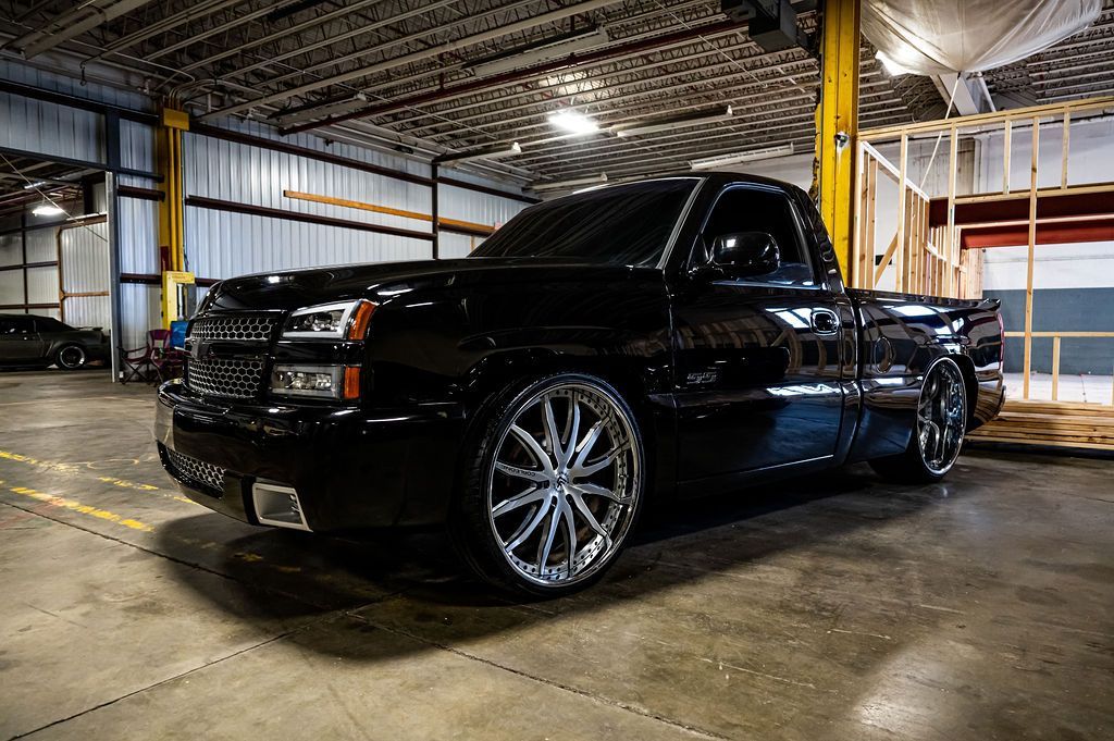 Black Chevrolet pickup truck with chrome rims in a garage.