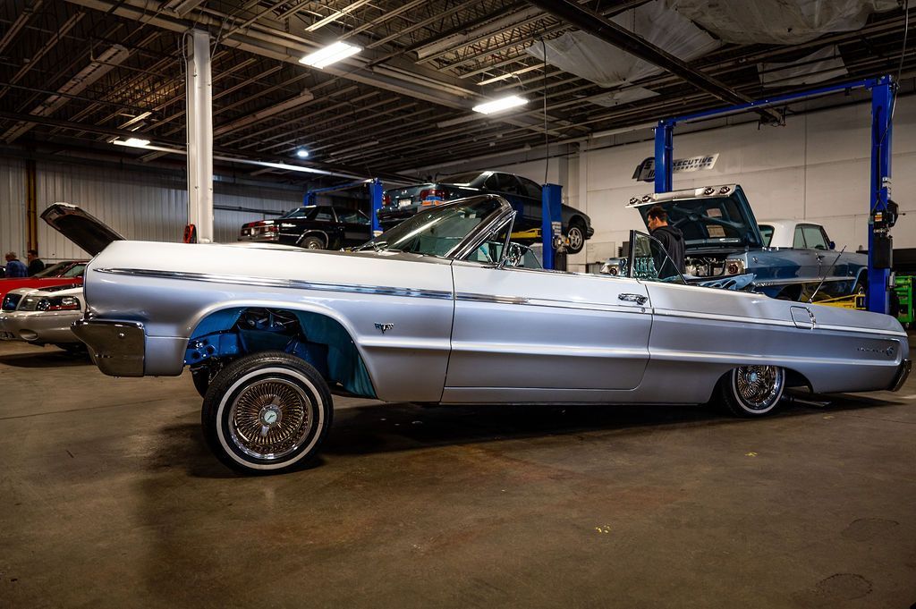 Silver lowrider convertible car inside a garage.