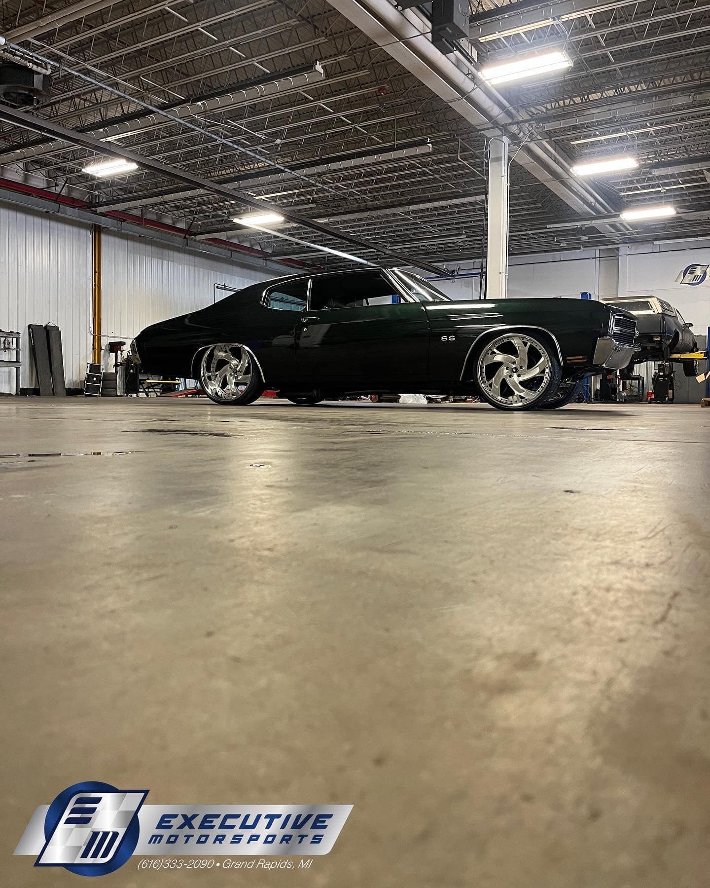 Black classic car parked inside a large garage with chrome wheels.