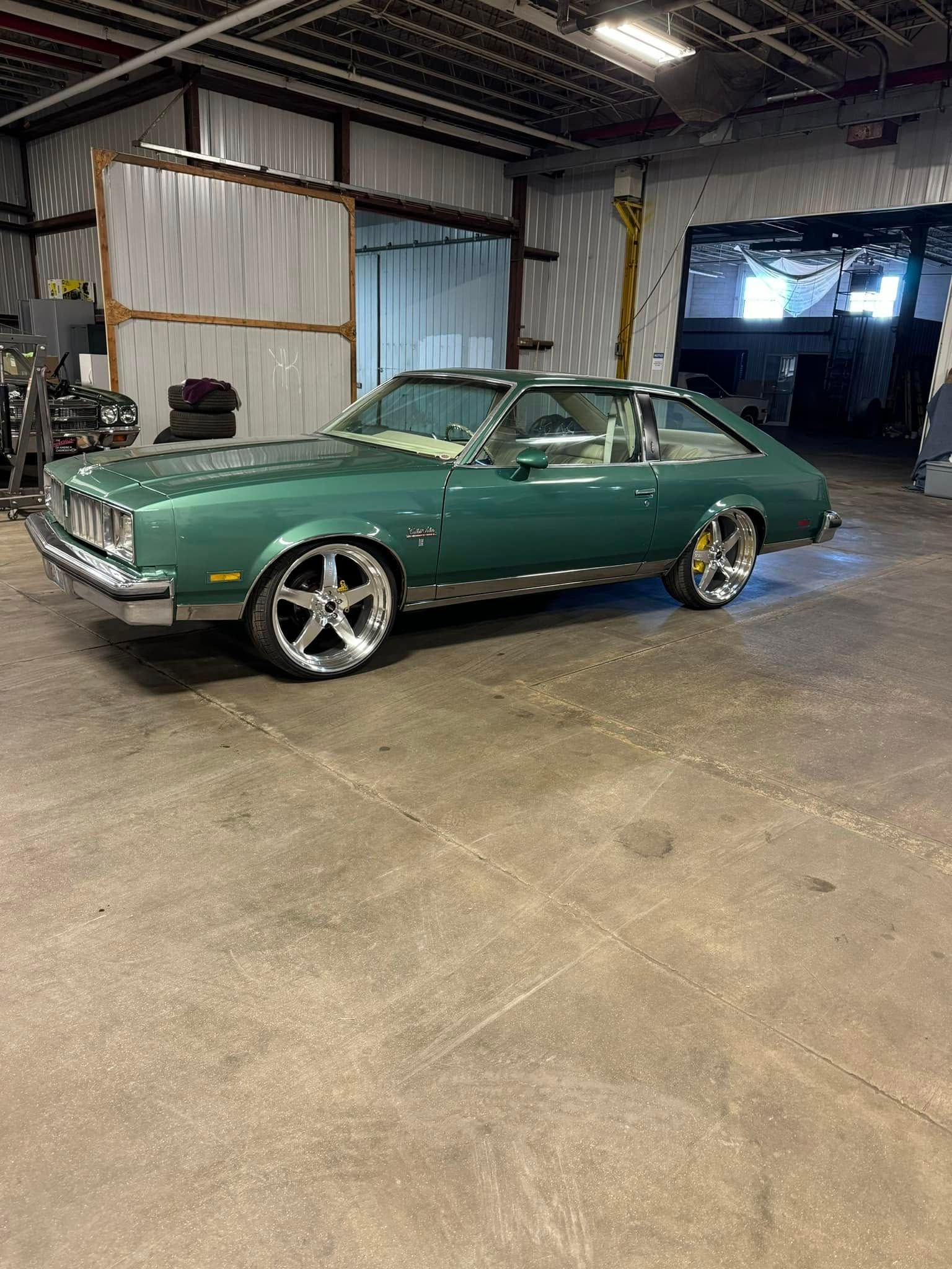 Green classic car with chrome wheels in a garage.