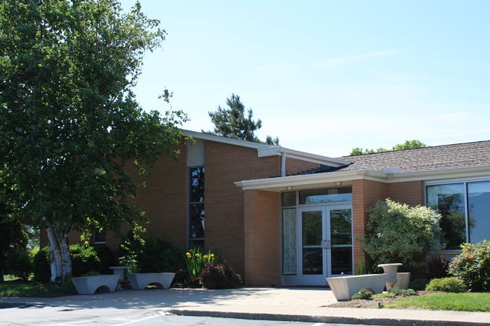 A brick building with a white door is surrounded by trees