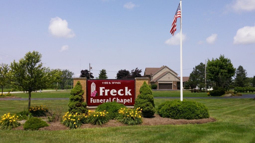 A sign for the freck funeral chapel with a flag in the background