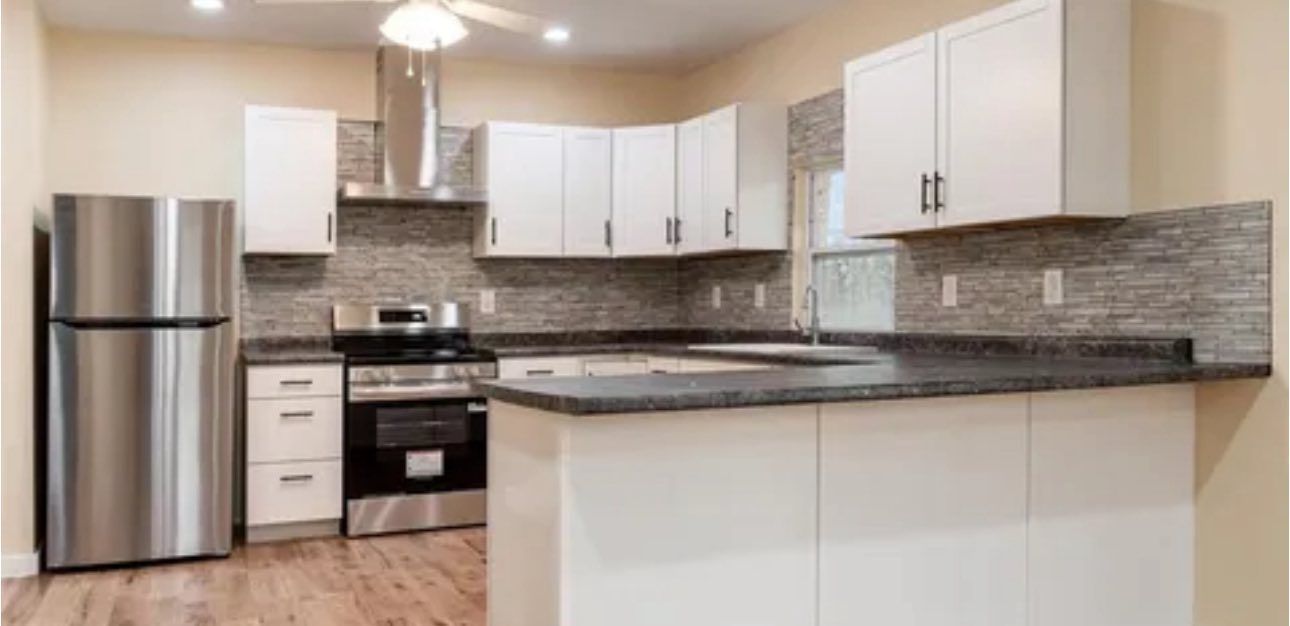 Modern kitchen with white cabinets, dark countertops, stainless steel appliances, and gray stone-style backsplash.