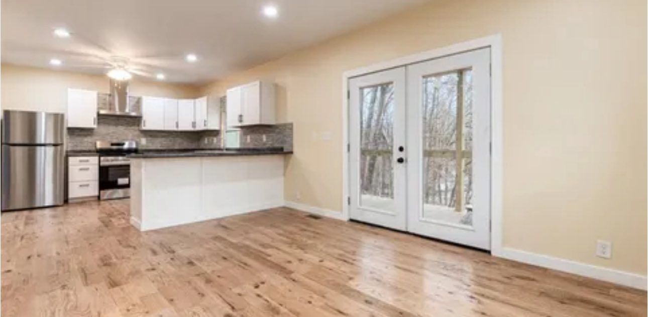 A modern kitchen with white cabinets, stainless steel appliances, and a wood floor next to a glass patio door.