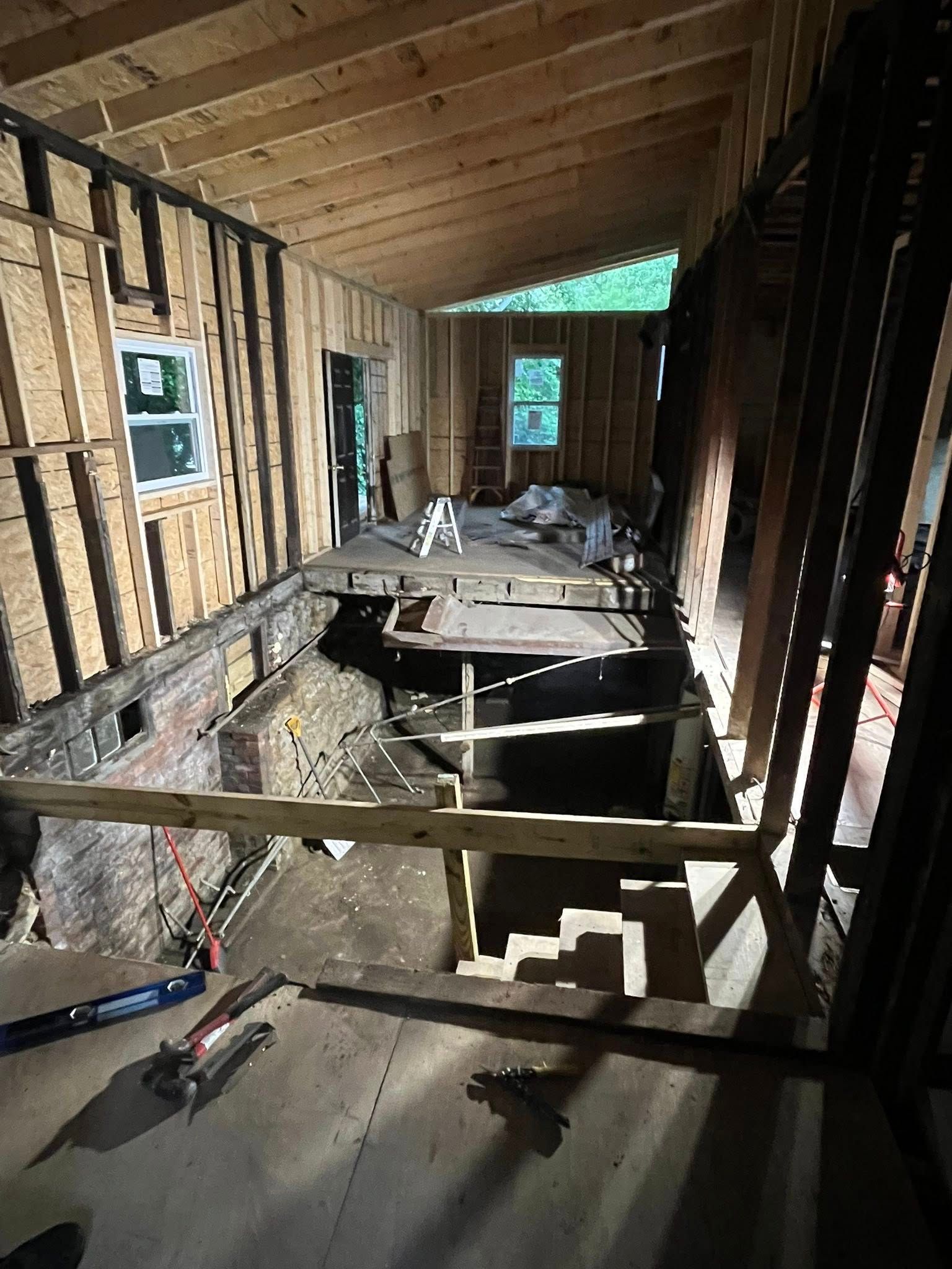 An interior view of a room under construction with exposed wooden wall studs, floor joists, and a partial subfloor.
