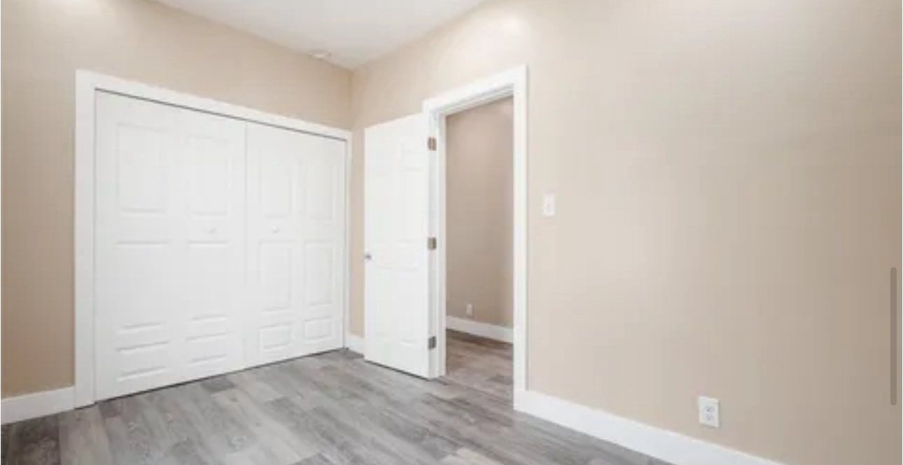 A room interior with beige walls, grey wood-look floors, a white sliding closet door, and an open doorway.