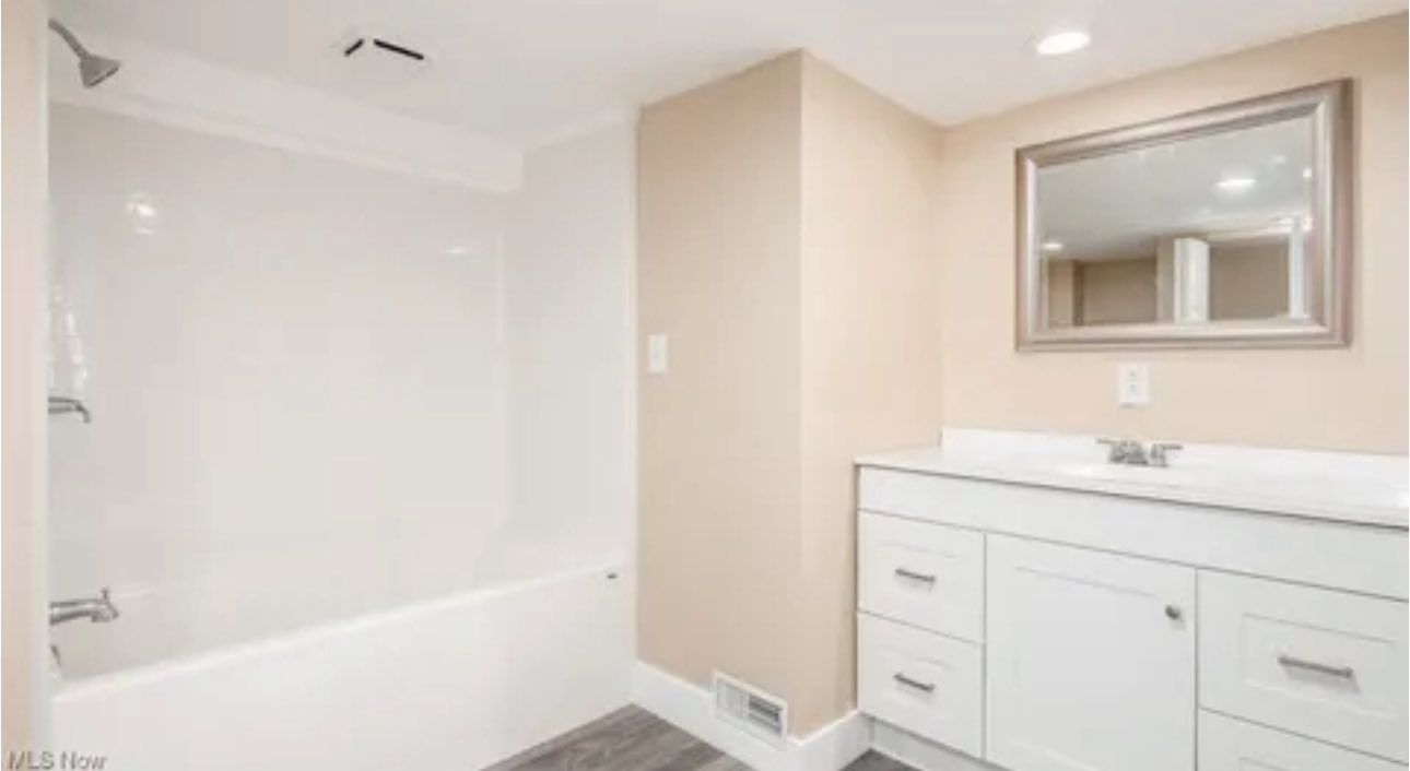 A modern bathroom featuring a white bathtub, a tiled shower wall, and a white vanity with a mirror above it.