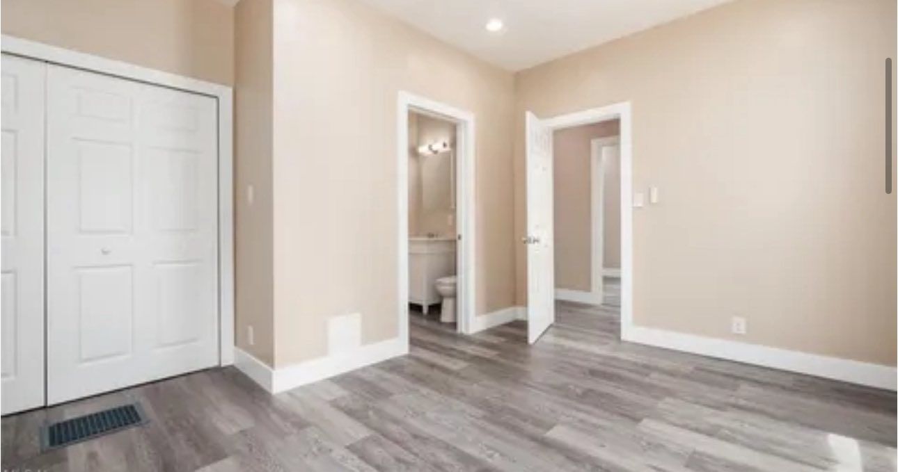 A view of a bright room with beige walls, grey wood-look flooring, white trim, a closet, and two open doorways.