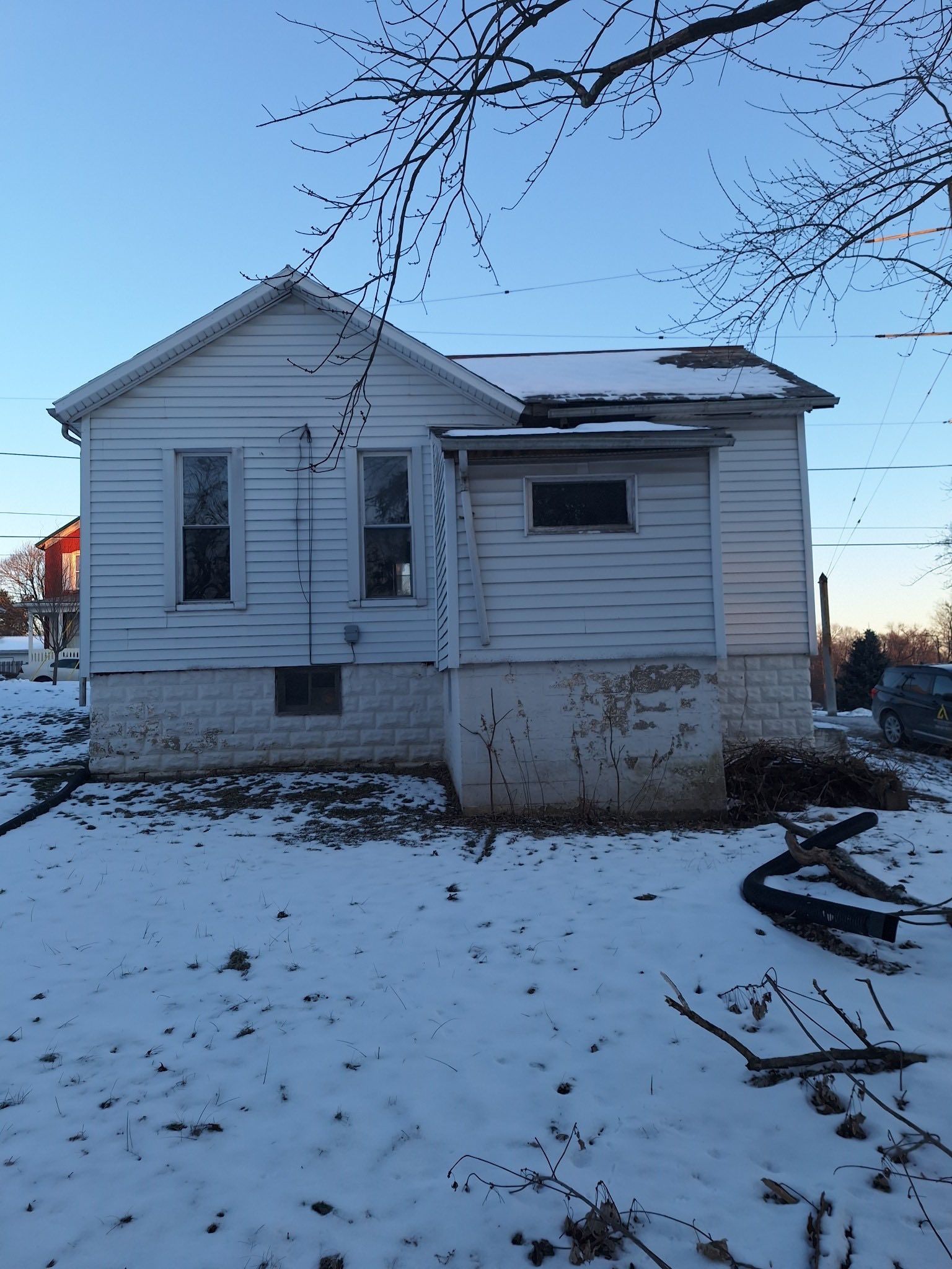 A small, white, single-story house with a snow-covered yard and roof under a clear blue sky.