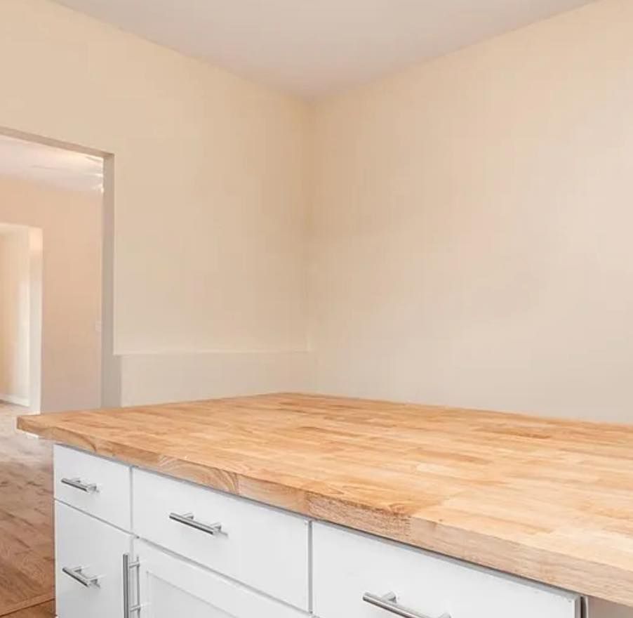 A kitchen island with a light-wood butcher block countertop and white cabinets, with an open doorway to another room.